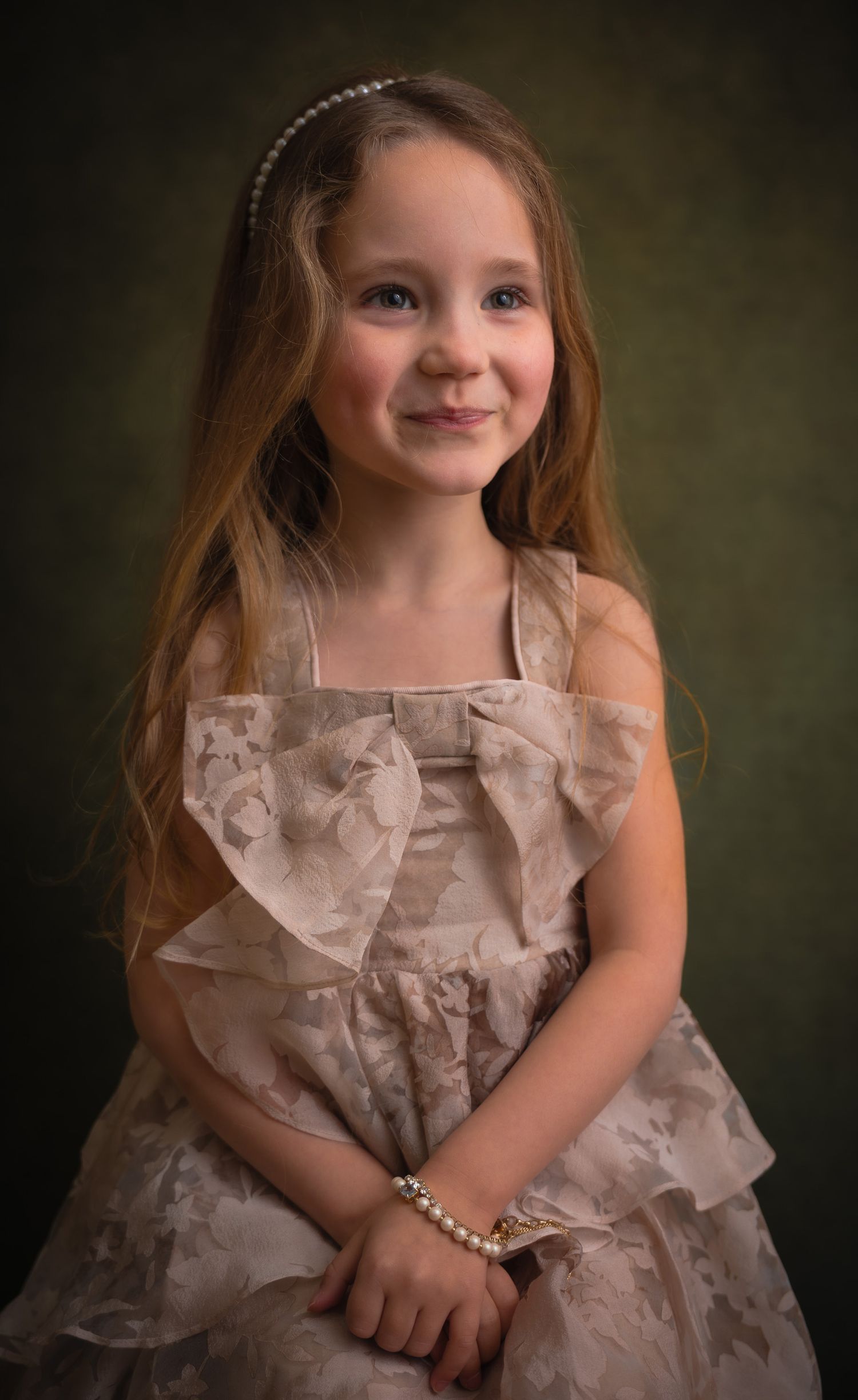 Young girl in elegant blush floral dress with pearl bracelet and headband smiling at camera against dark background made in my photostudio.