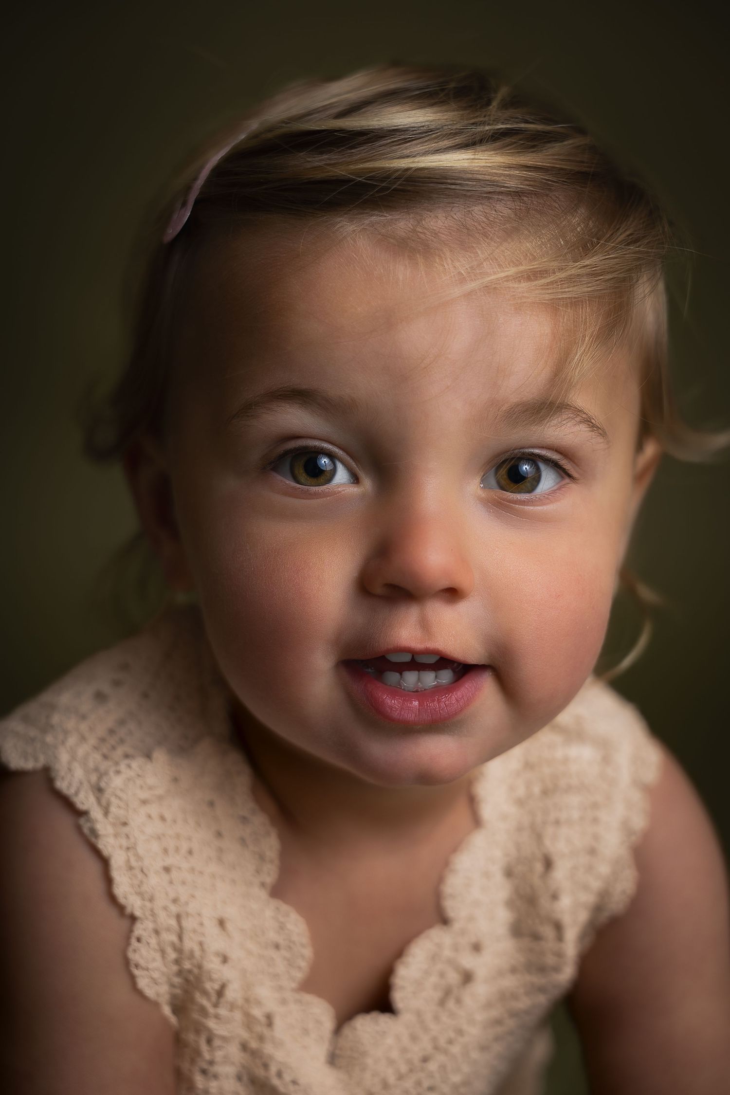 Close-up portrait of a cute toddler girl in cream knit outfit with a playful expression.