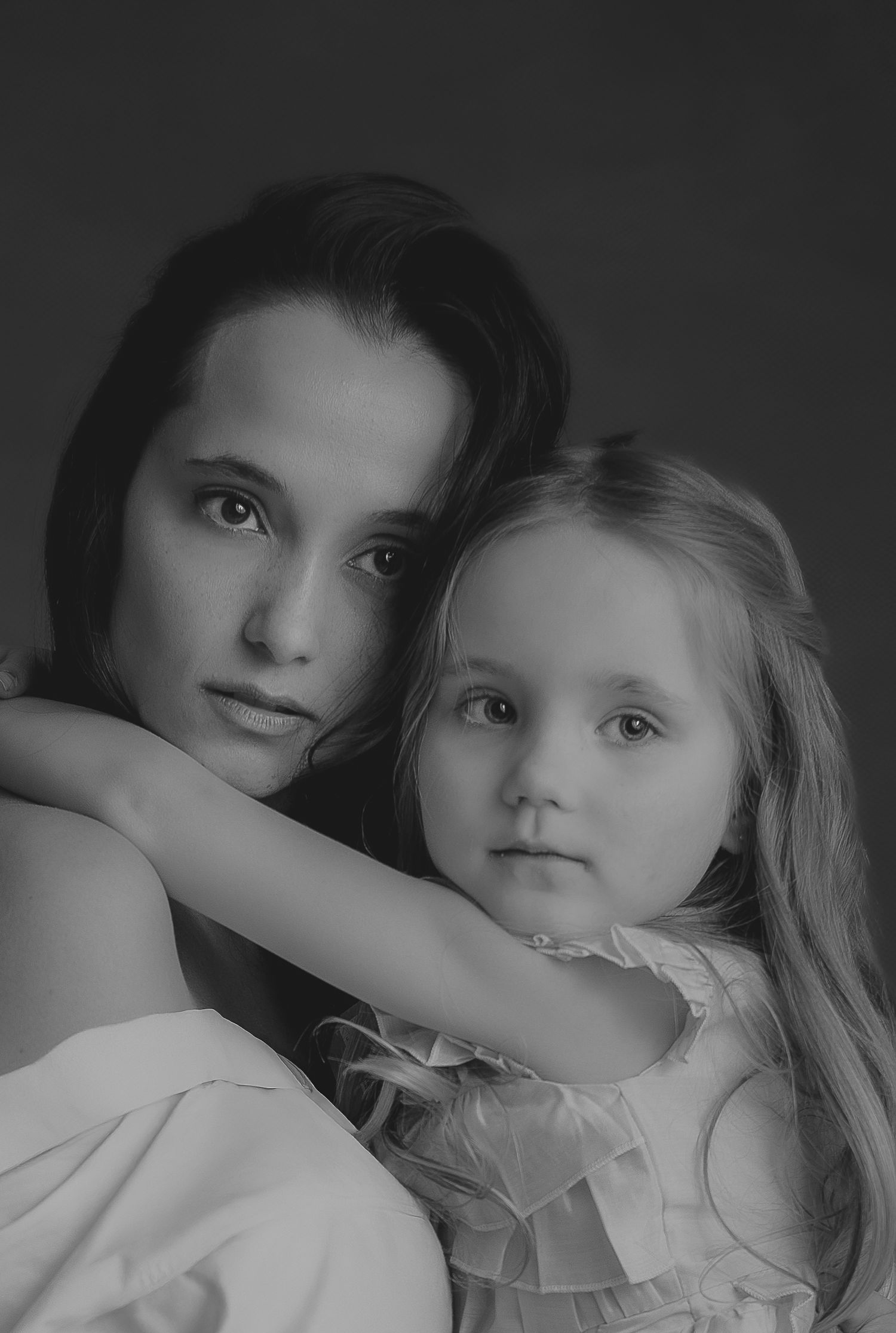 Zwart-wit portret van een moeder en dochter die elkaar teder vasthouden in de fotostudio.