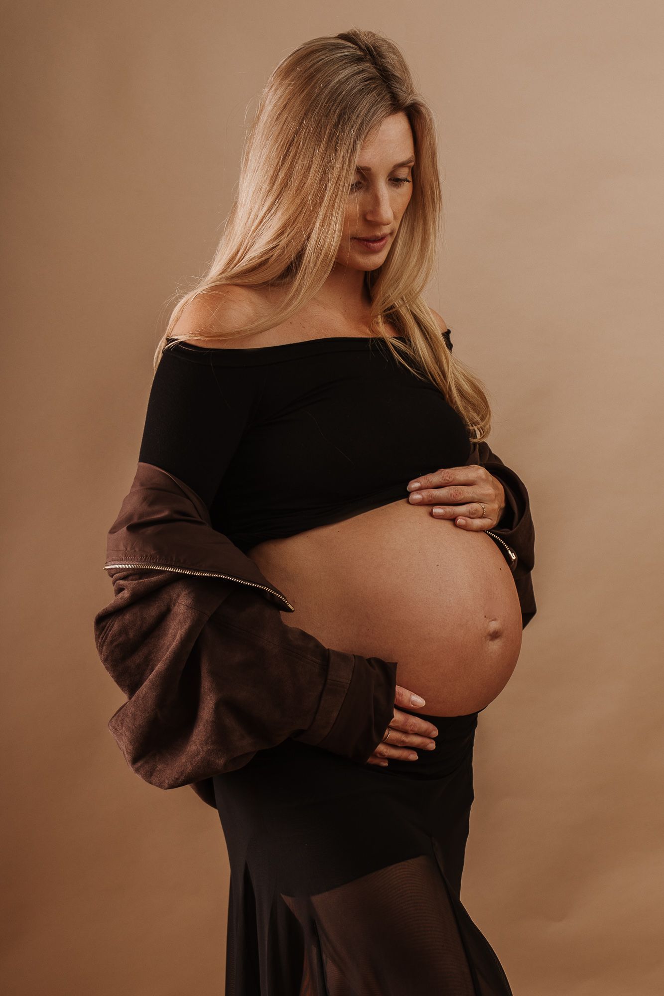 Zwangere vrouw in zwarte top en bruine blazer tijdens zwangerschapsshoot in studio Assen