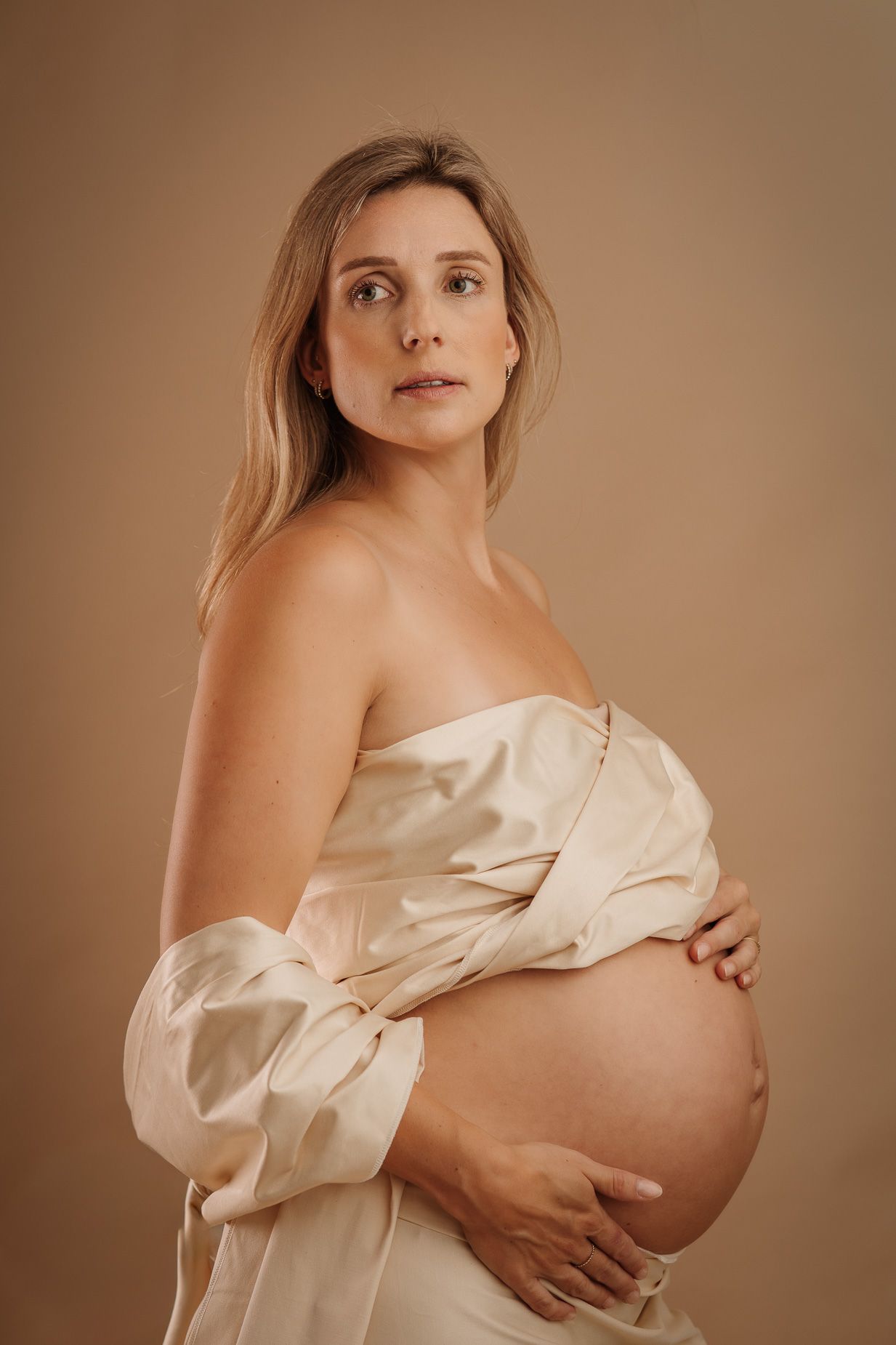 Zwangere vrouw in crèmekleurige satijnen doek tijdens zwangerschapsshoot bij Mini Mellow