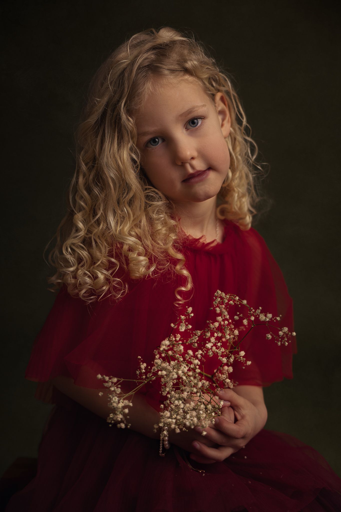 Kinderportret van een meisje met blonde krullen in een rode jurk met sierlijke decoratieve takken.