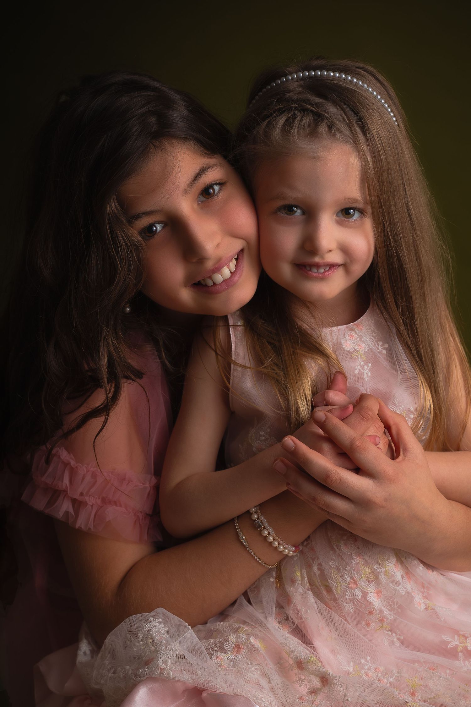 Kinderportret van twee zusjes in roze jurken die elkaar knuffelen en samen naar de camera lachen.