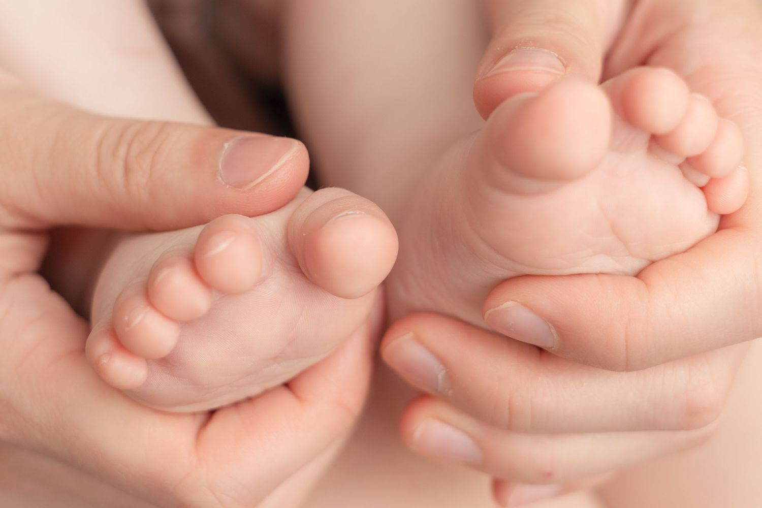 Adult hands gently cradling tiny newborn baby feet, showcasing the delicate size difference in a tender close-up photo.