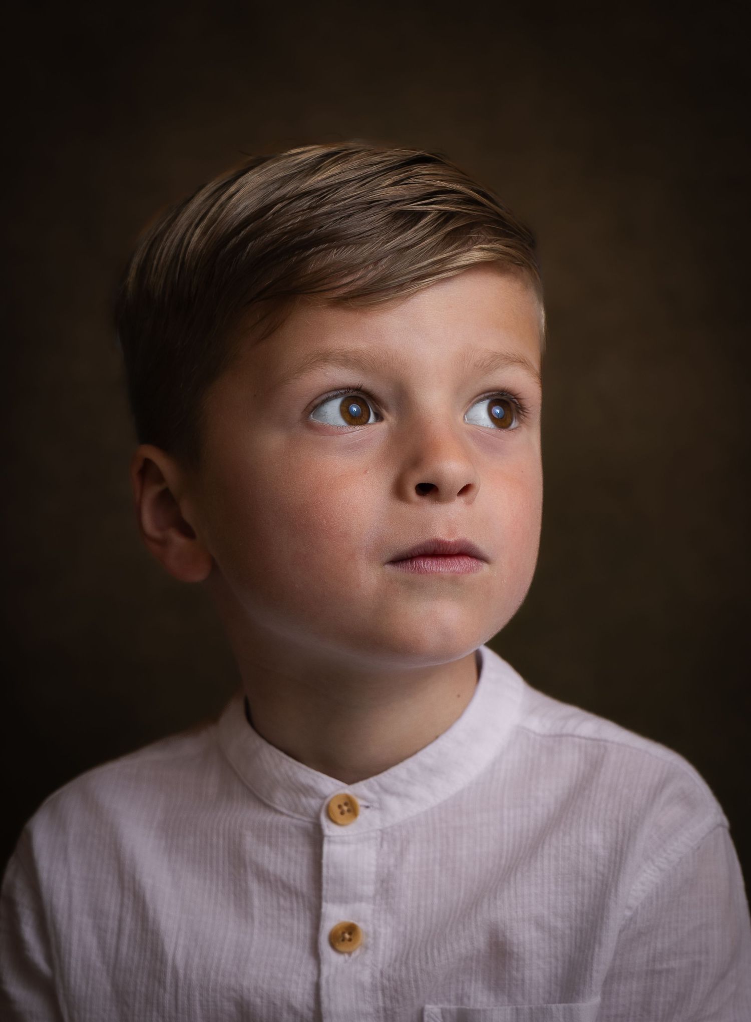 Kinderportret van een jonge jongen in een wit overhemd met een donkere studioachtergrond.