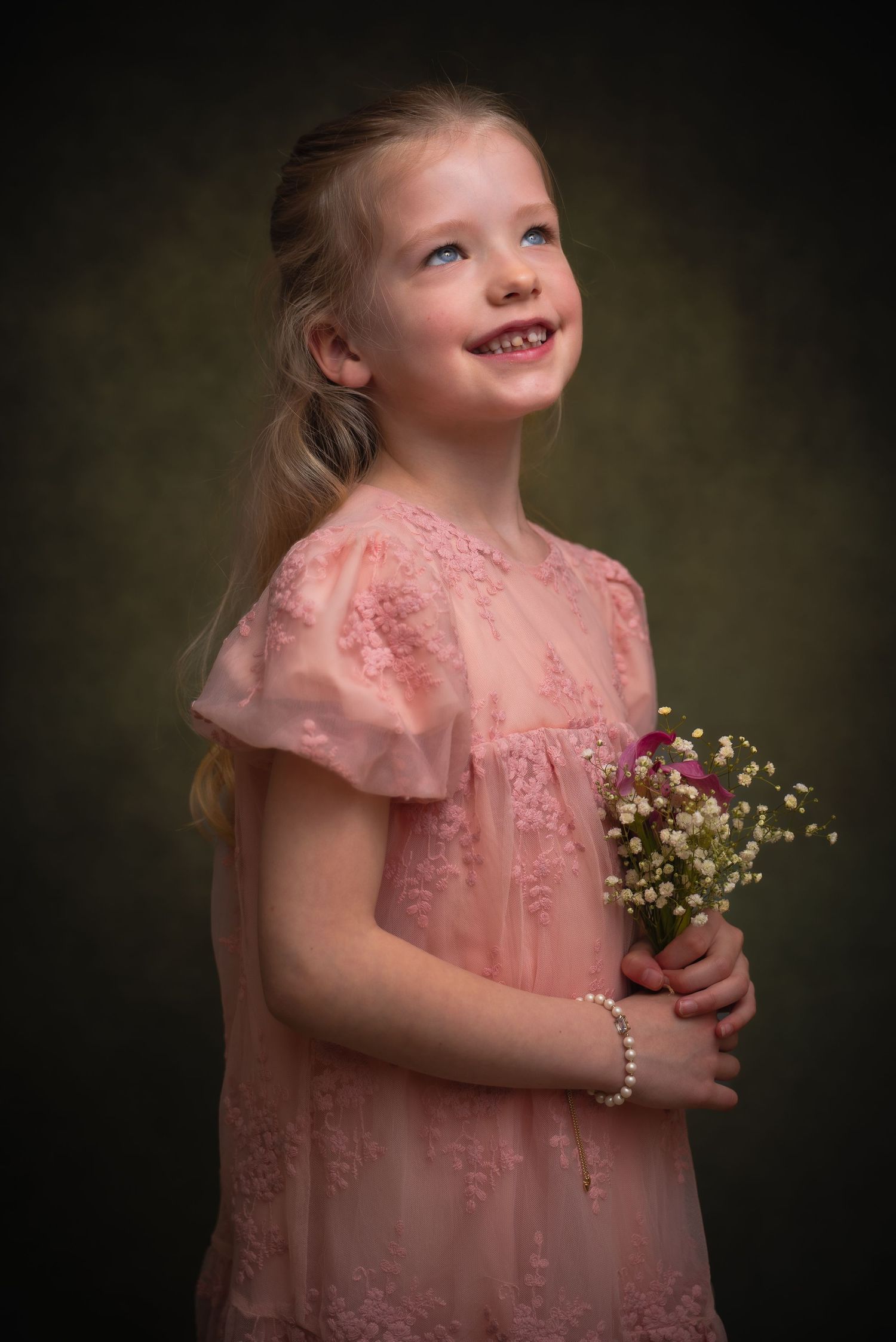 Kinderportret van een glimlachend meisje in een roze kanten jurk met een boeketje wilde bloemen.