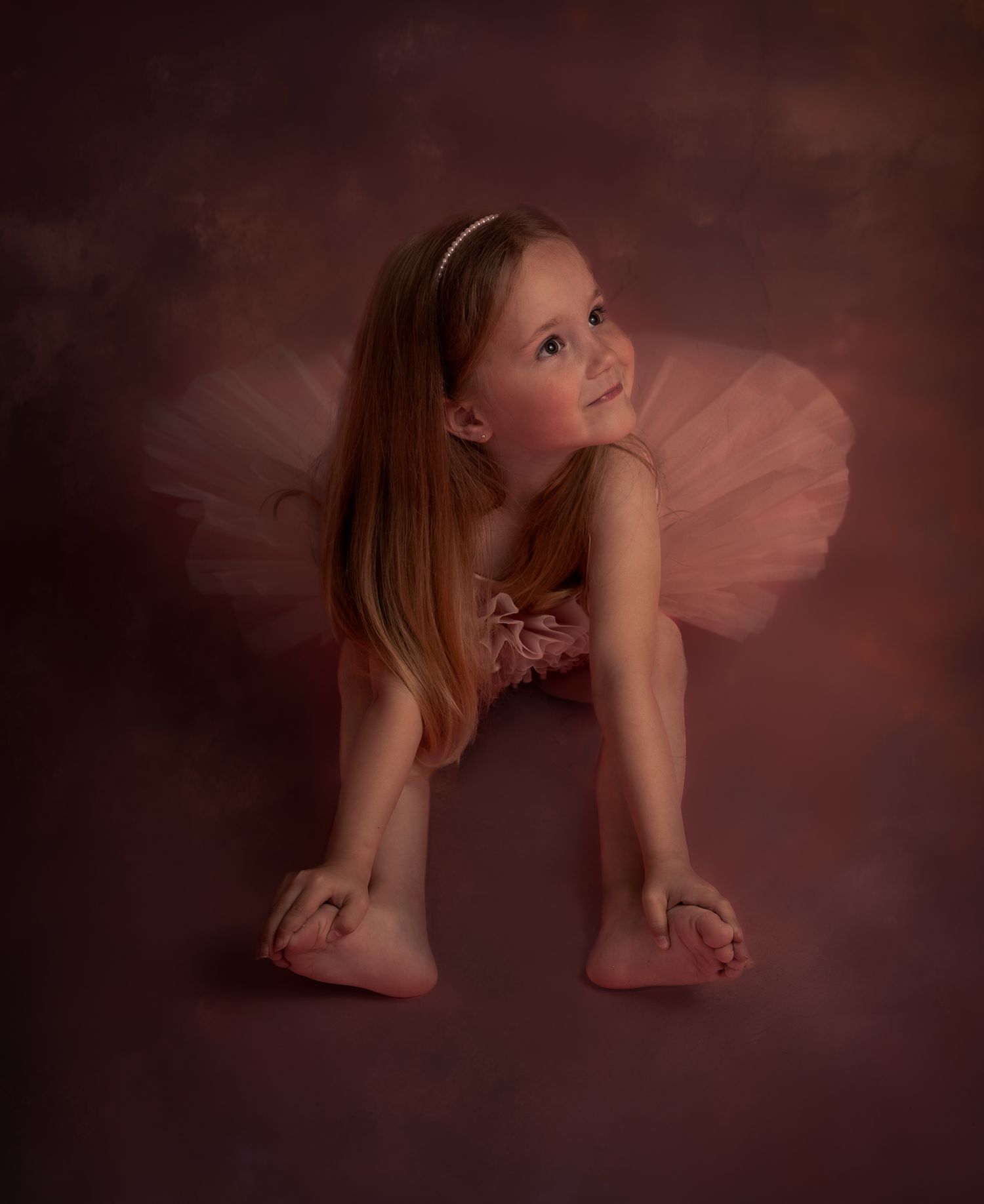 Kinderportret van een jonge ballerina in een roze tutu tegen een donkere studioachtergrond.