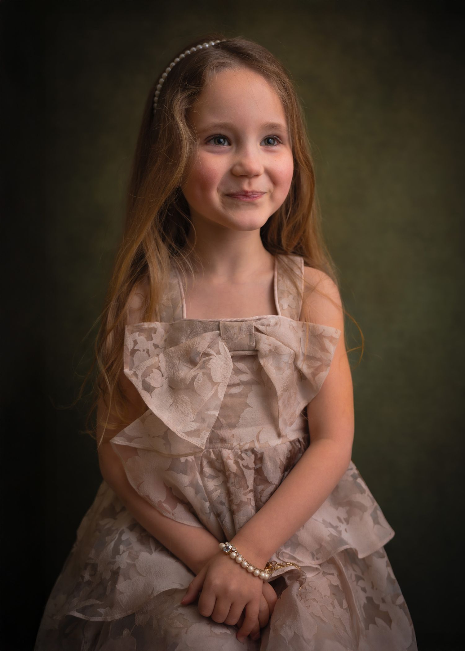 Klassiek kinderportret van een jong meisje met lang bruin haar, een elegante beige jurk en parelaccessoires.