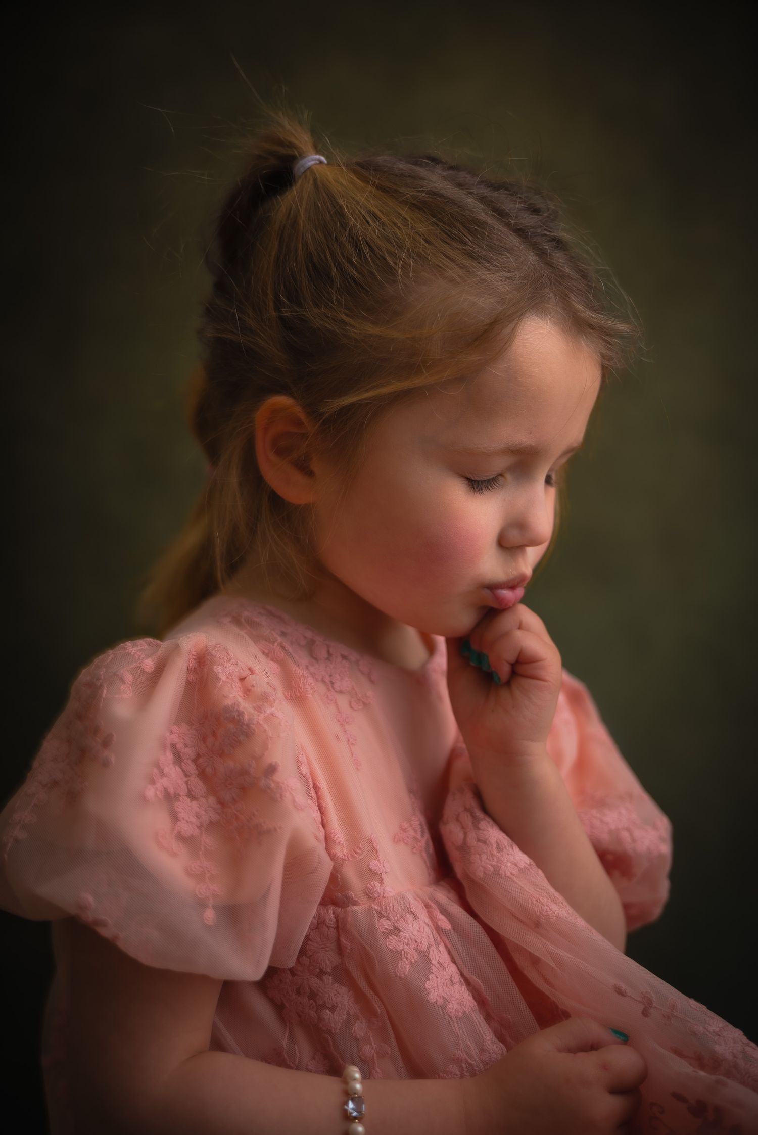 Kinderportret van een meisje in een roze kanten jurk met een parelarmband en een rustige blik naar beneden.
