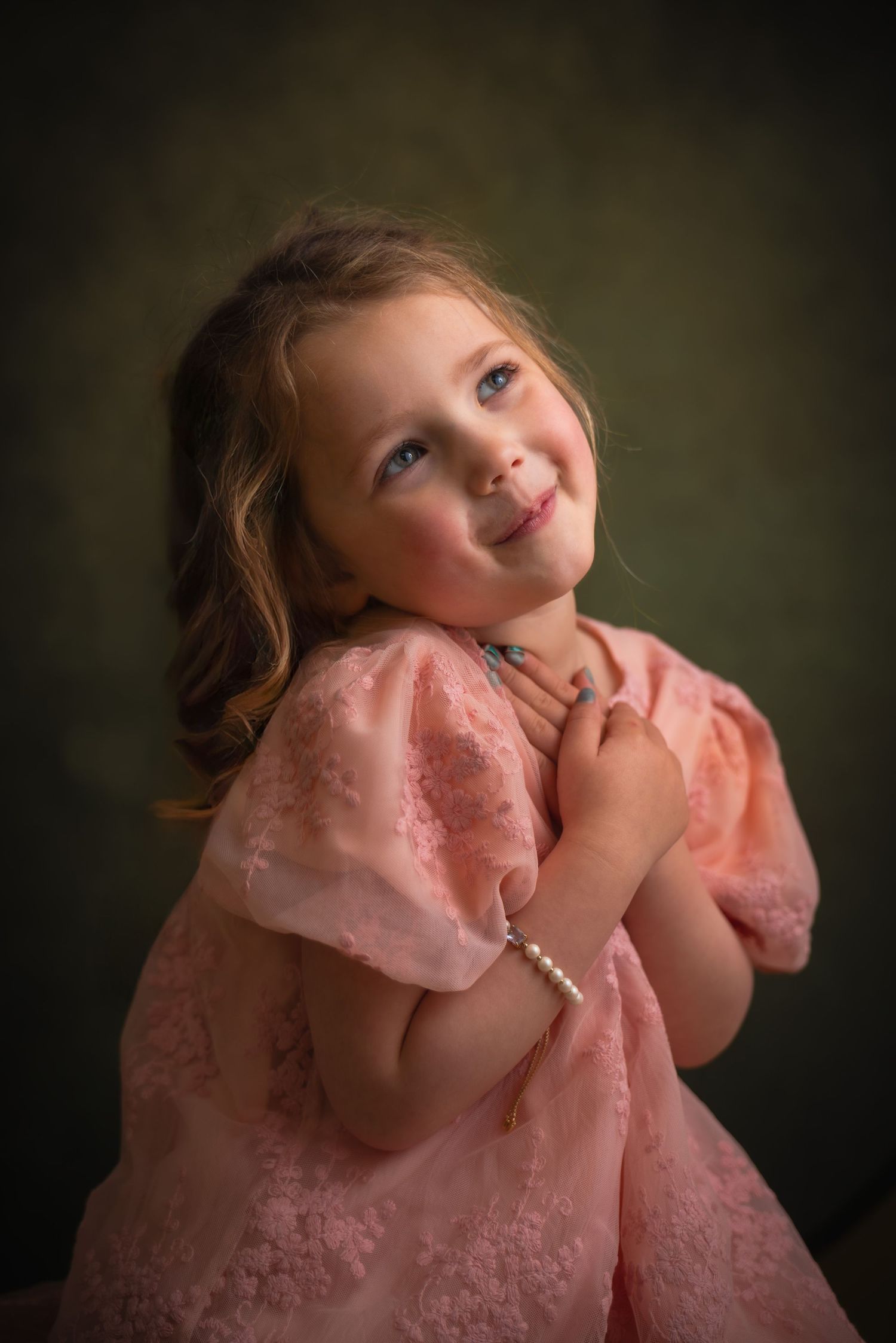 Charming little girl in pink lace dress with pearl bracelet poses playfully in a professional studio portrait.
