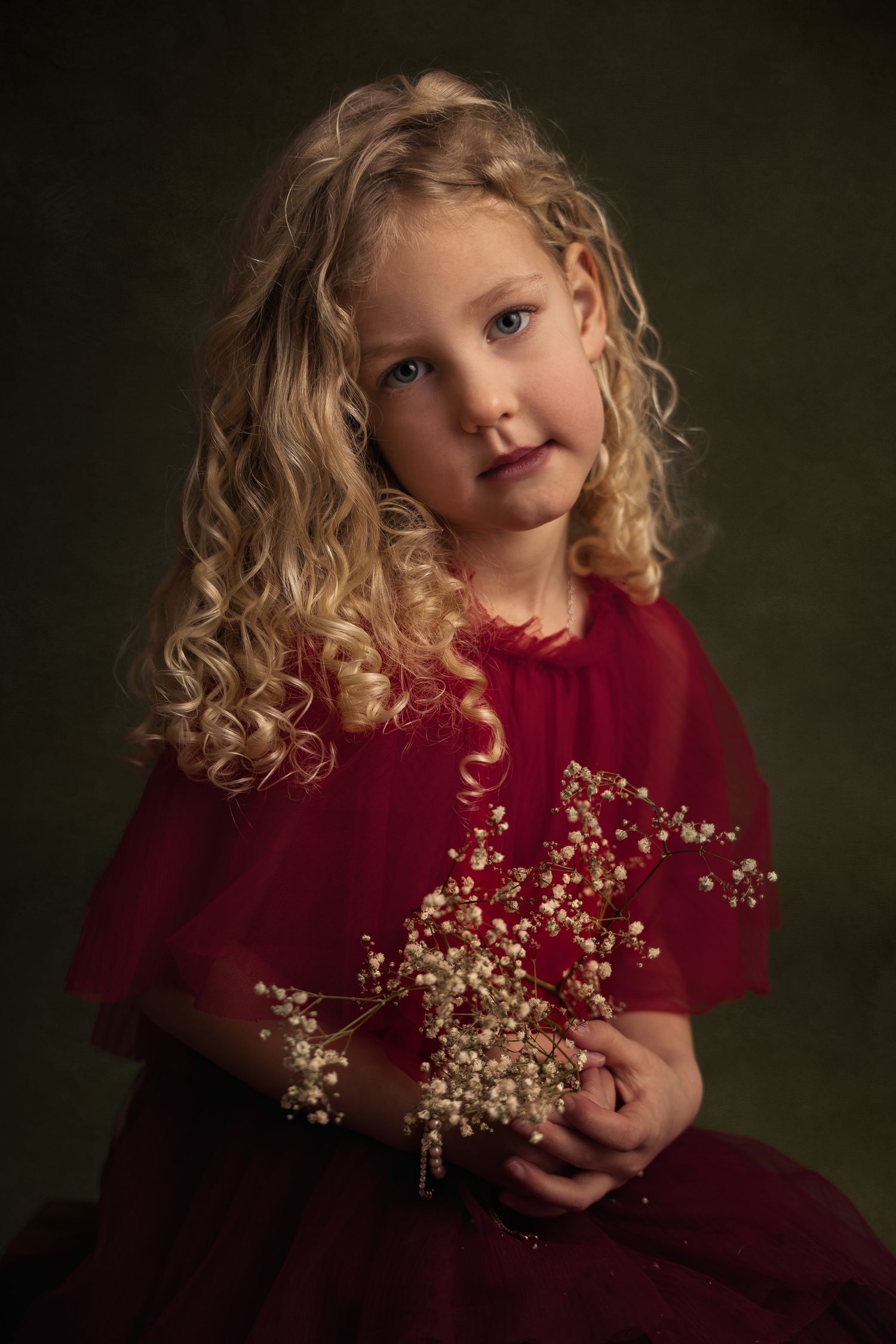 Fine-art kinderportret van een jong meisje met blonde krullen in een rode jurk met gedroogde parelbloemen.