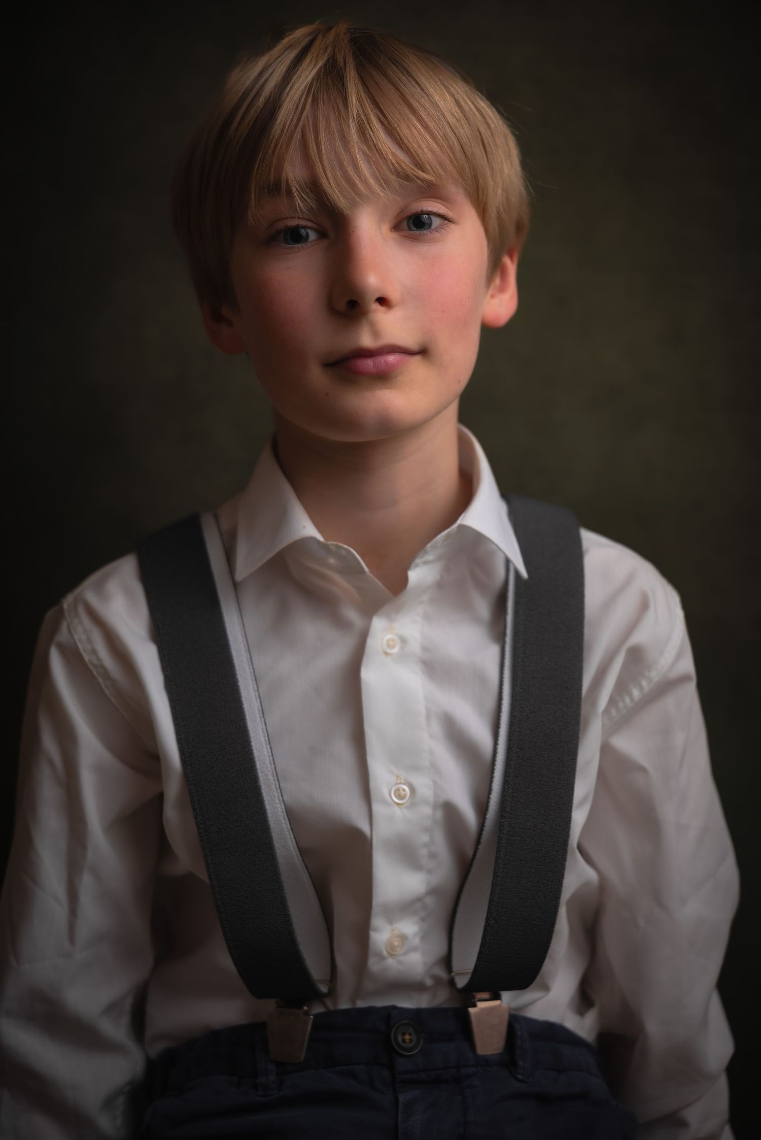 Fine-art kinderportret van een blonde jongen in een wit overhemd en grijze bretels.