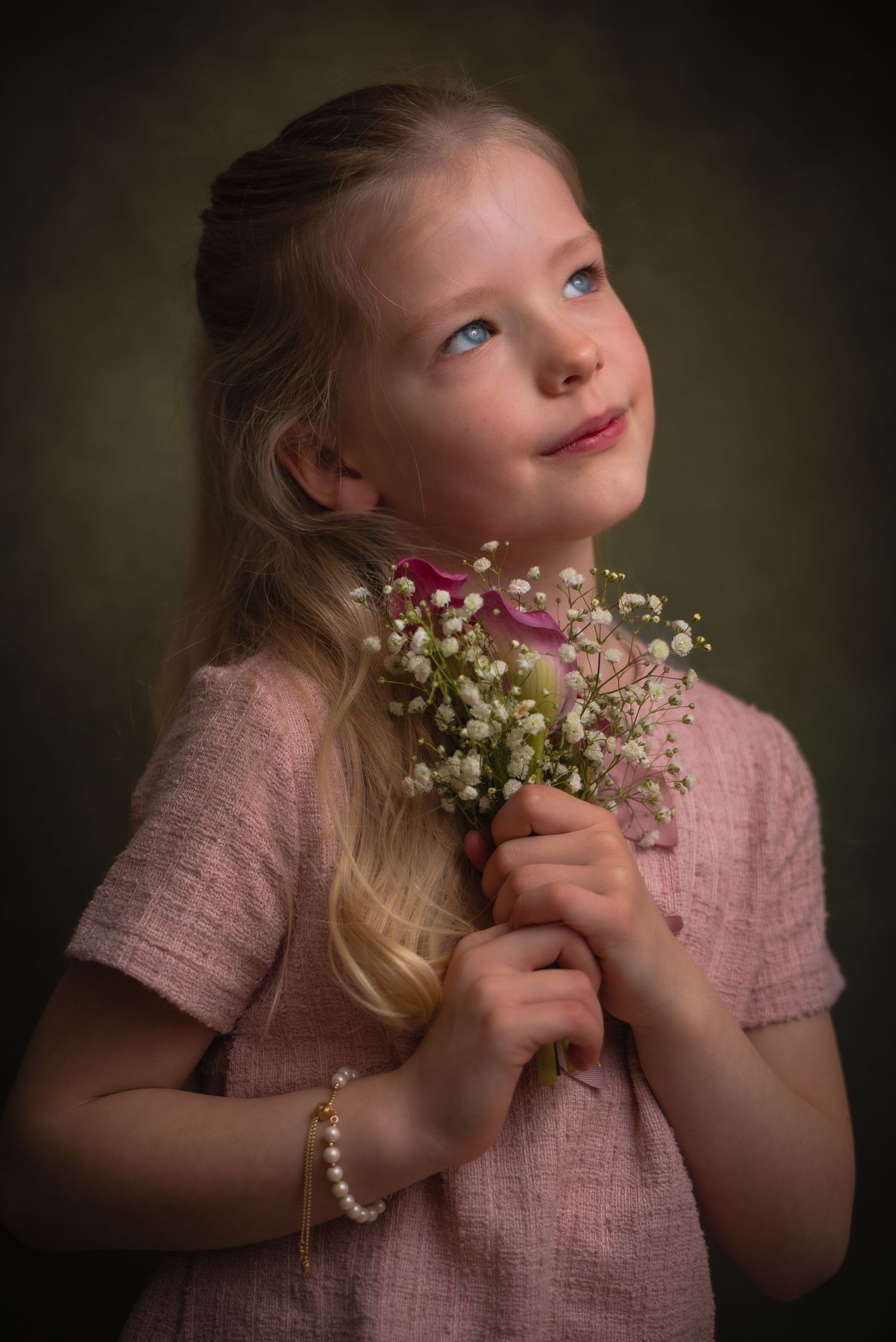 Klassiek kinderportret van een blond meisje in een roze jurk met witte bloemen en een dromerige blik omhoog.