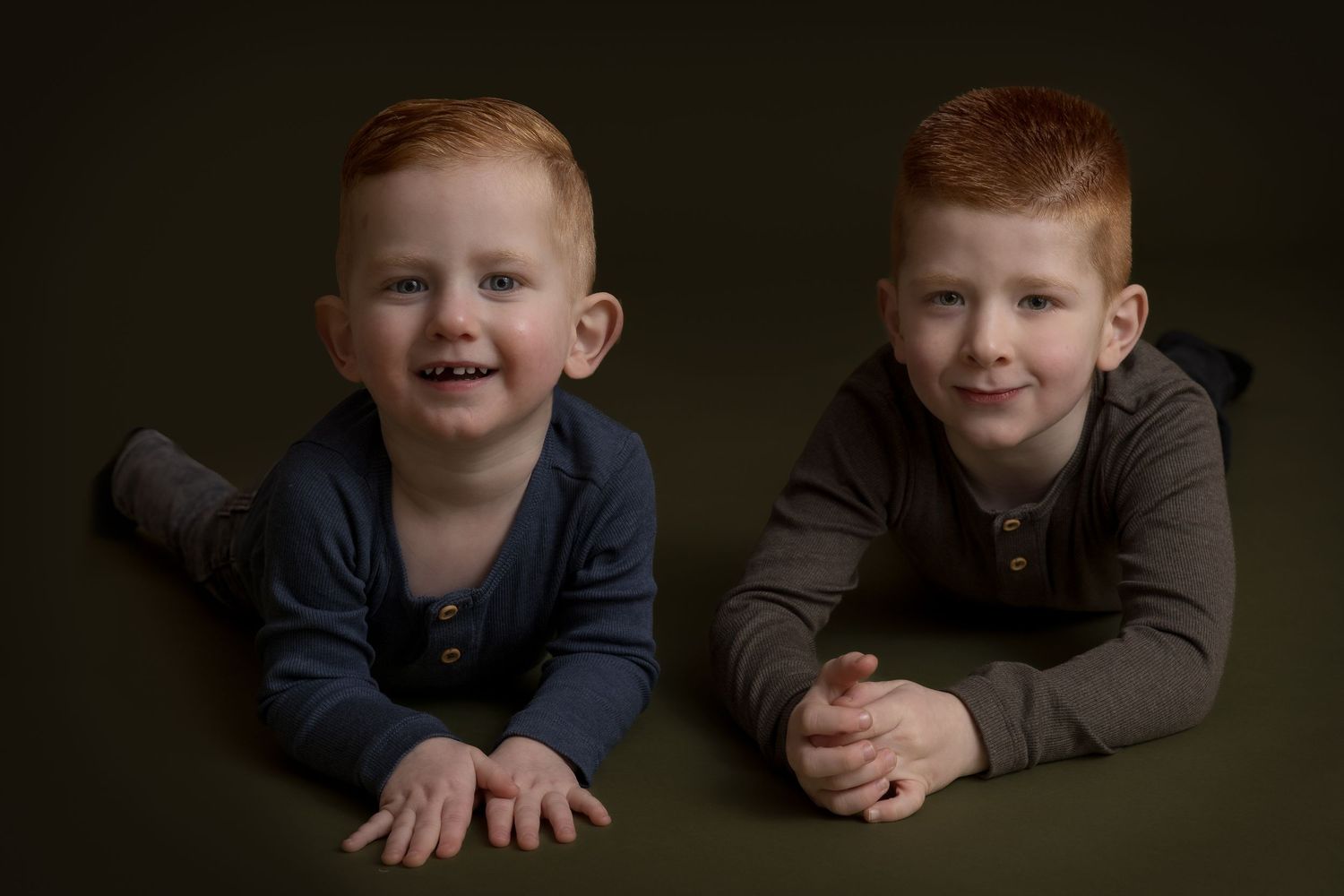 Kinderportret van twee roodharige broers die samen glimlachen tegen een donkergroene achtergrond.