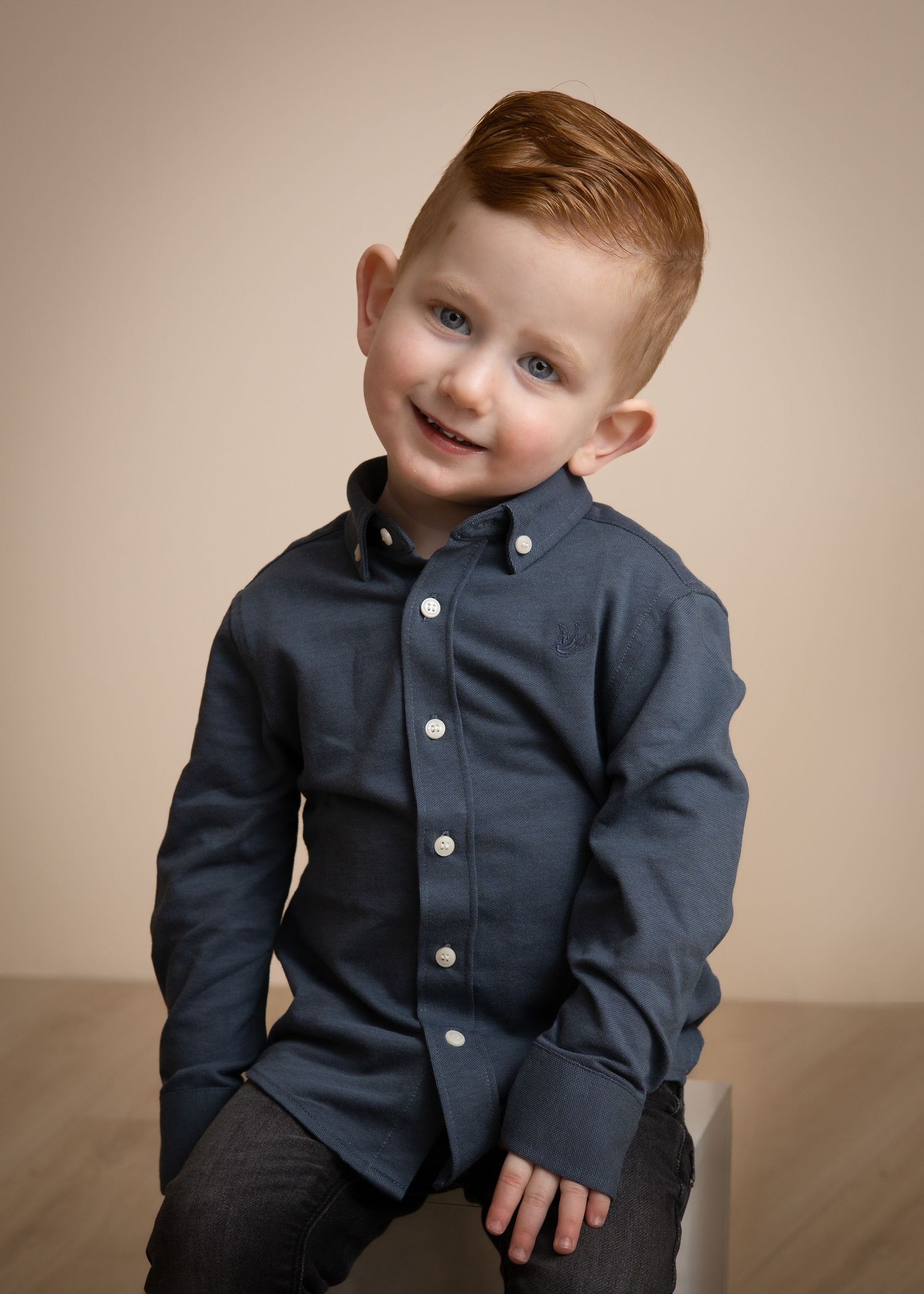 Professioneel kinderportret van een glimlachende roodharige jongen in een donkerblauw overhemd.