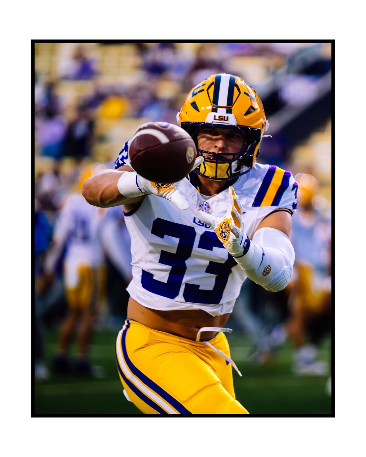 LSU football player in a white and yellow uniform focus-locked on catching a football mid-air during a game.