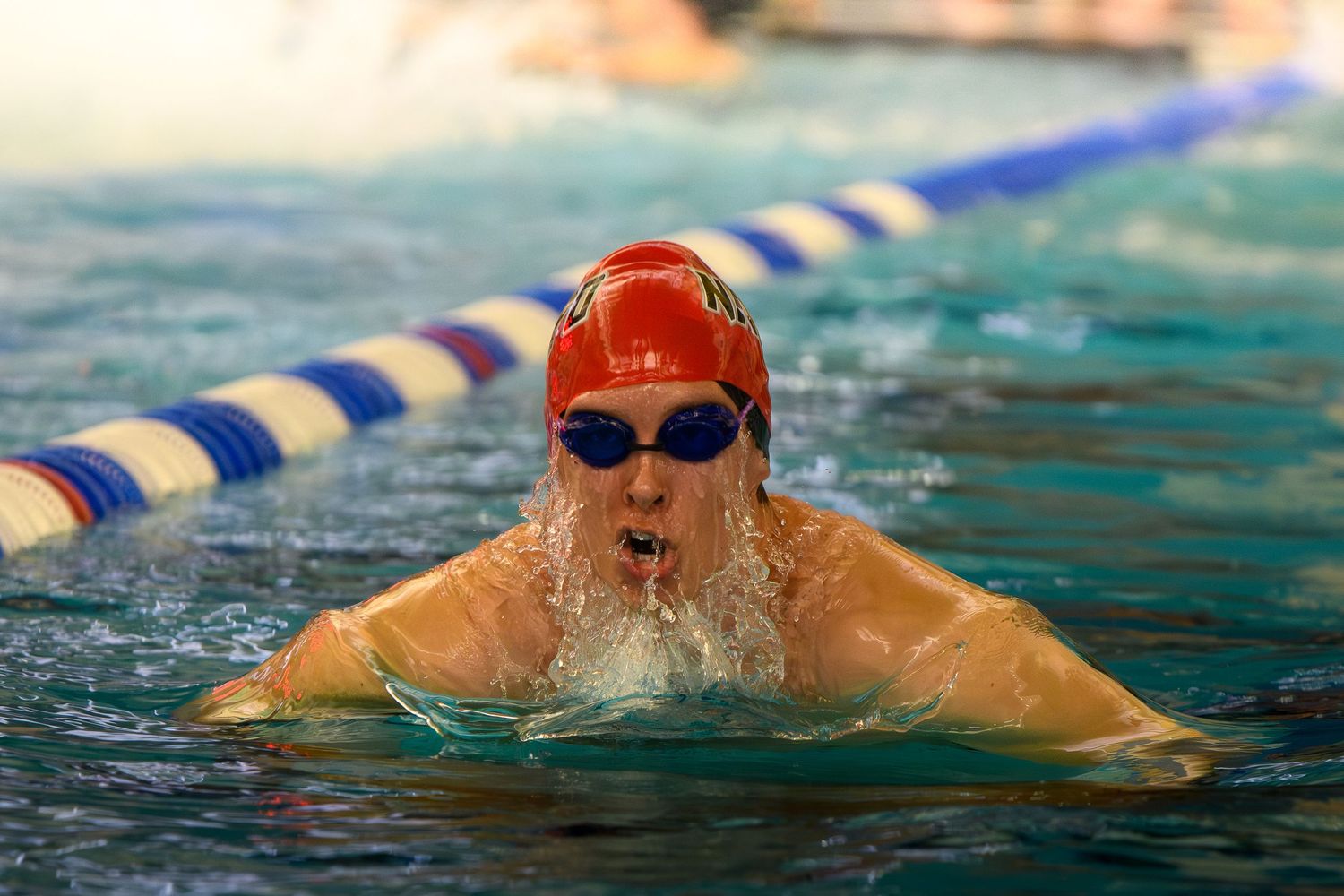 Competitive swimmer in a red cap surfacing for air while racing in an indoor swimming pool.