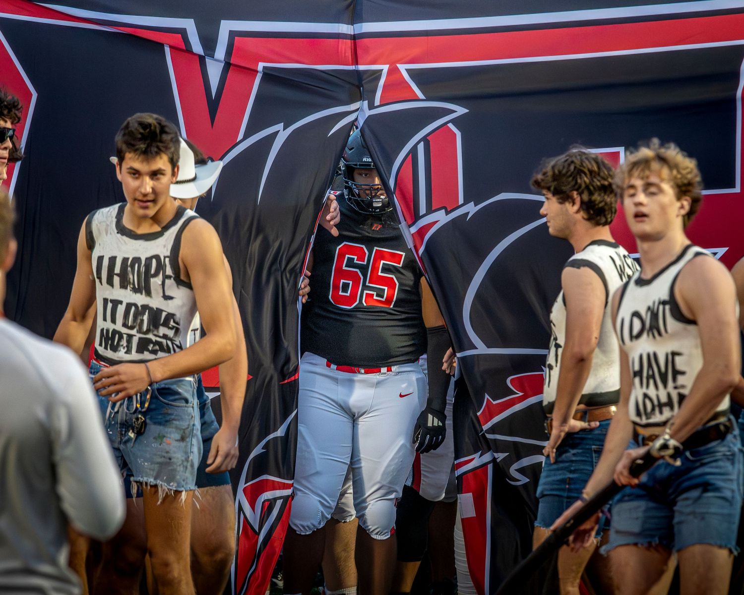 High school football player in a black and red jersey bursting through a paper banner at the start of a game.
