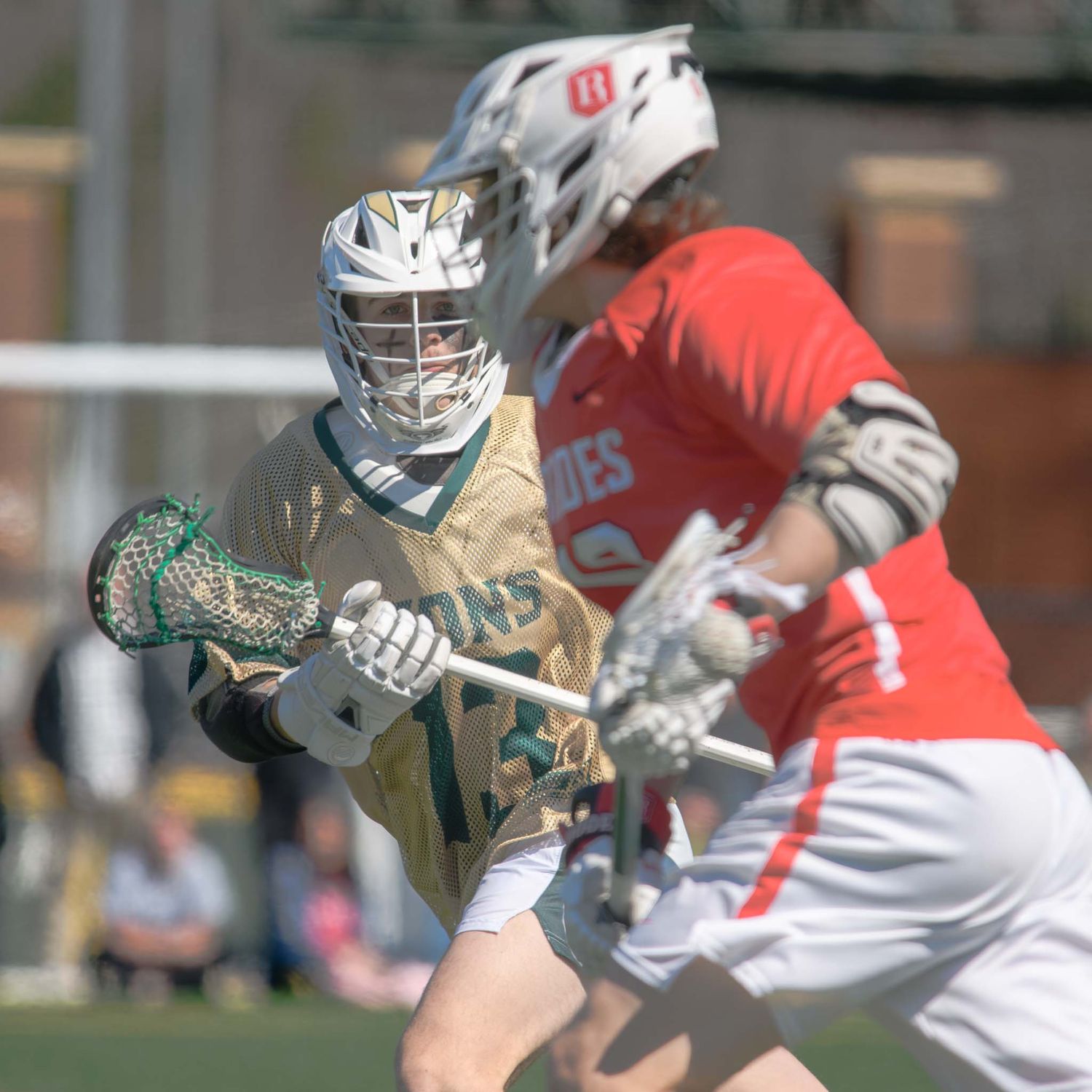 A lacrosse player in a white and blue uniform prepares a shot on goal while under pressure from a defender.