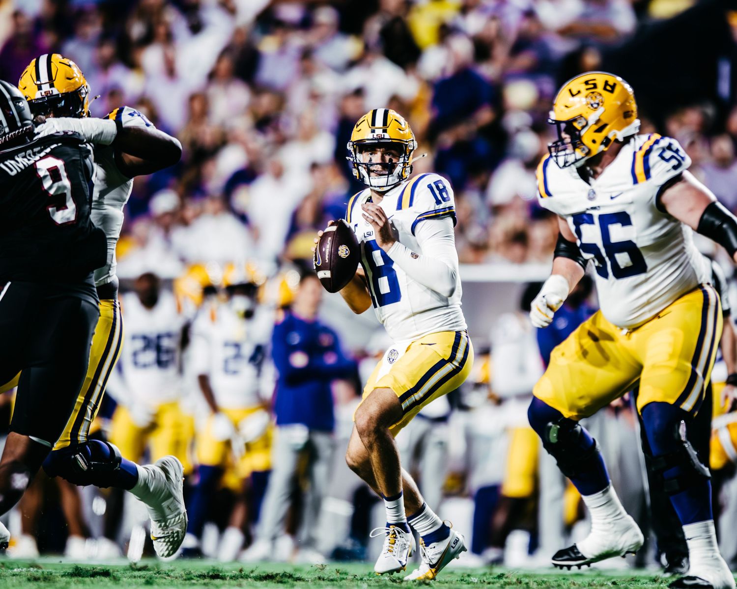 Action shot of an LSU quarterback in a white jersey looking for a receiver downfield during a night game.