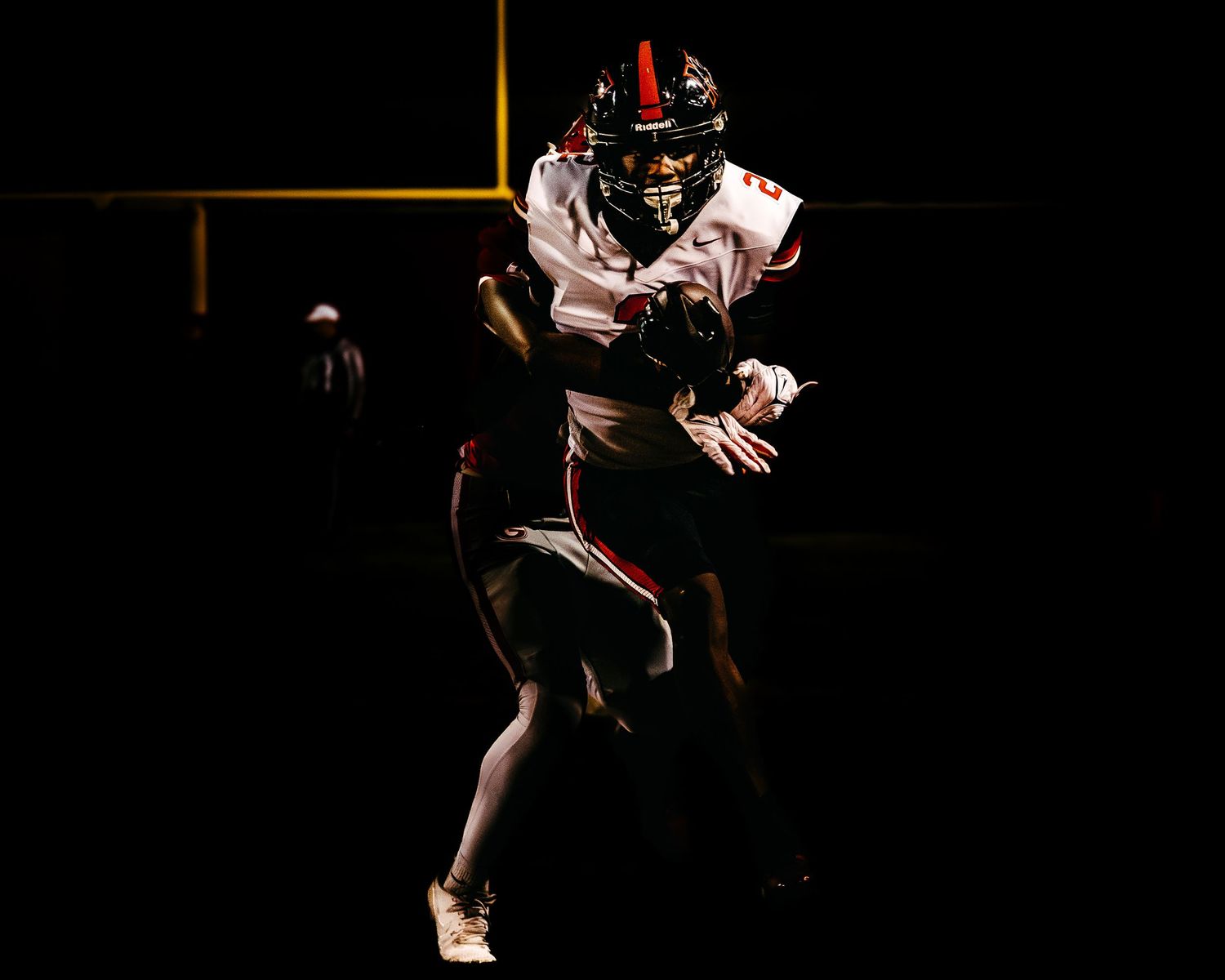 Dramatic low-key action shot of a football player in a white and black uniform running with the ball against a dark background.