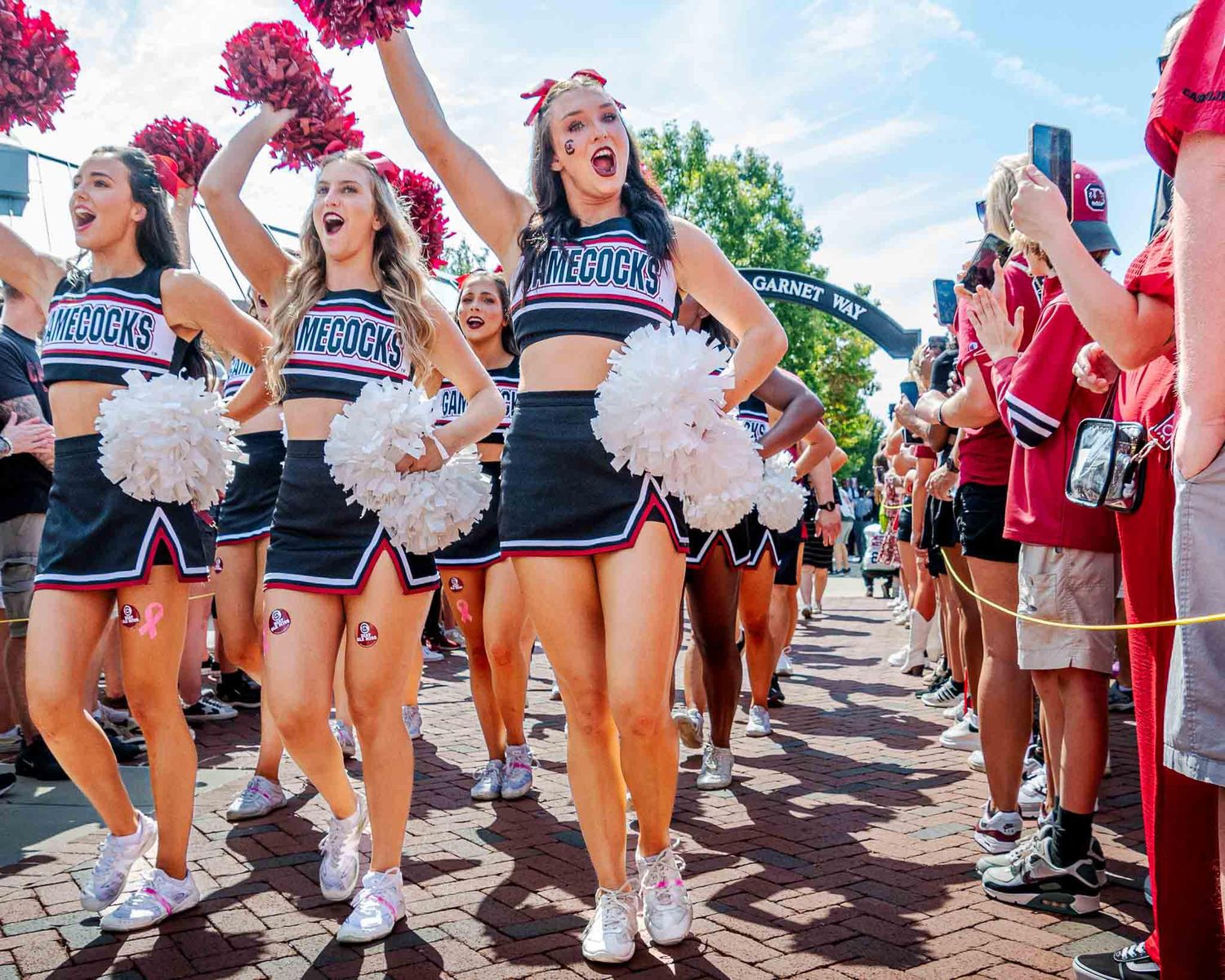 South Carolina Gamecocks cheerleaders lead a procession through a crowd of fans on a sunny game day.