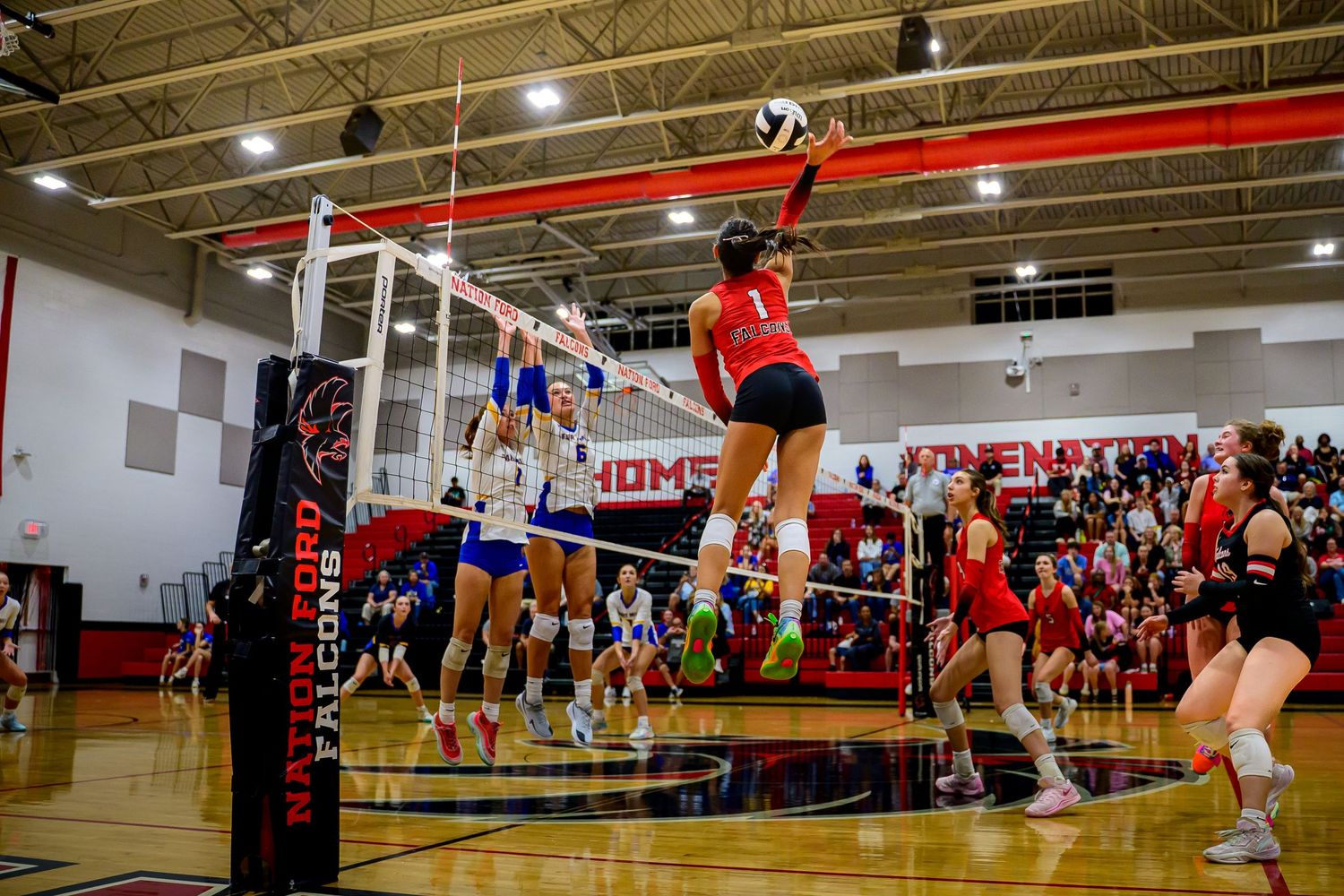 High-energy shot of a high school volleyball player jumping for a powerful spike over the net during a match.