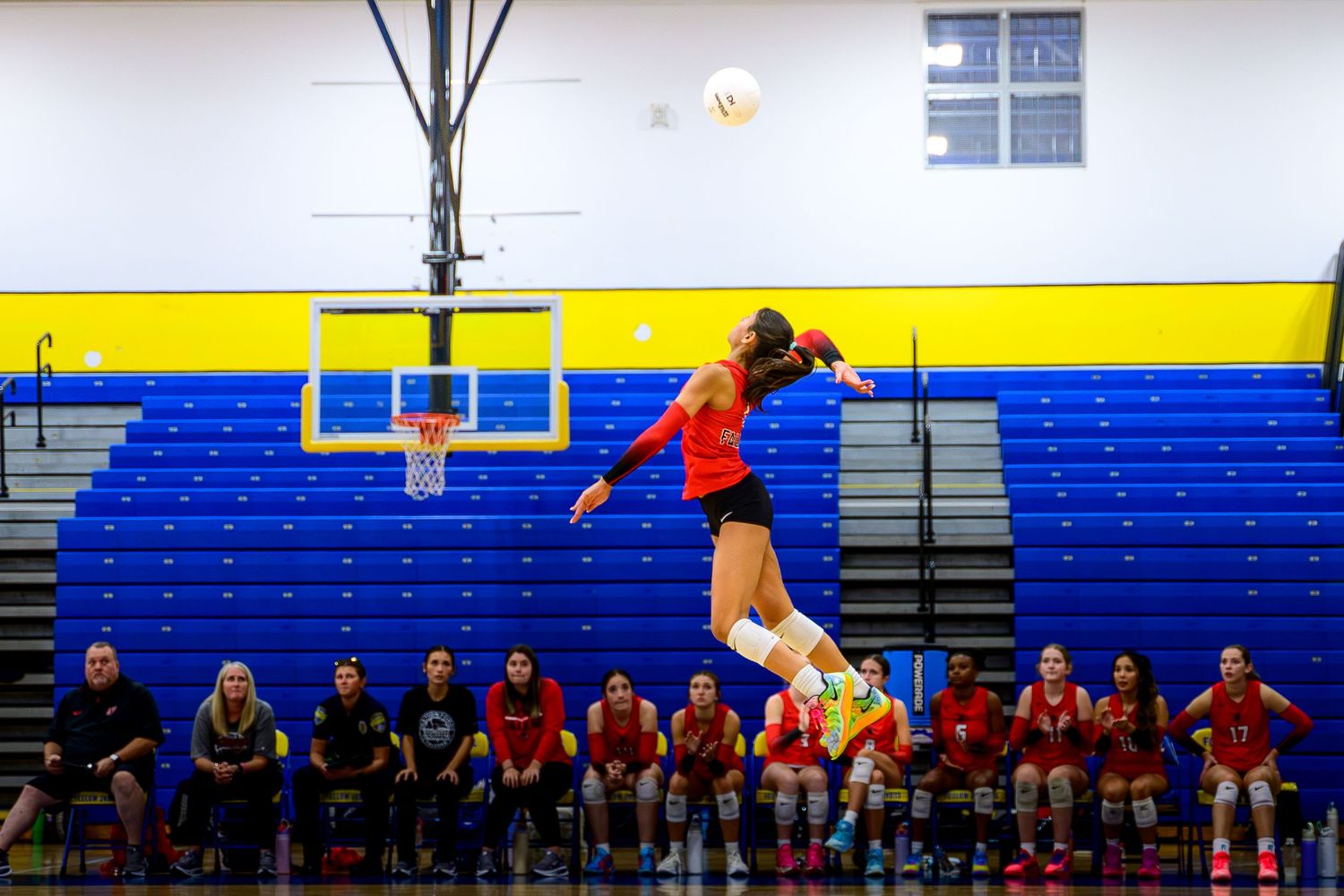High-action volleyball shot of a player in a red jersey mid-air while spiking the ball over the net.