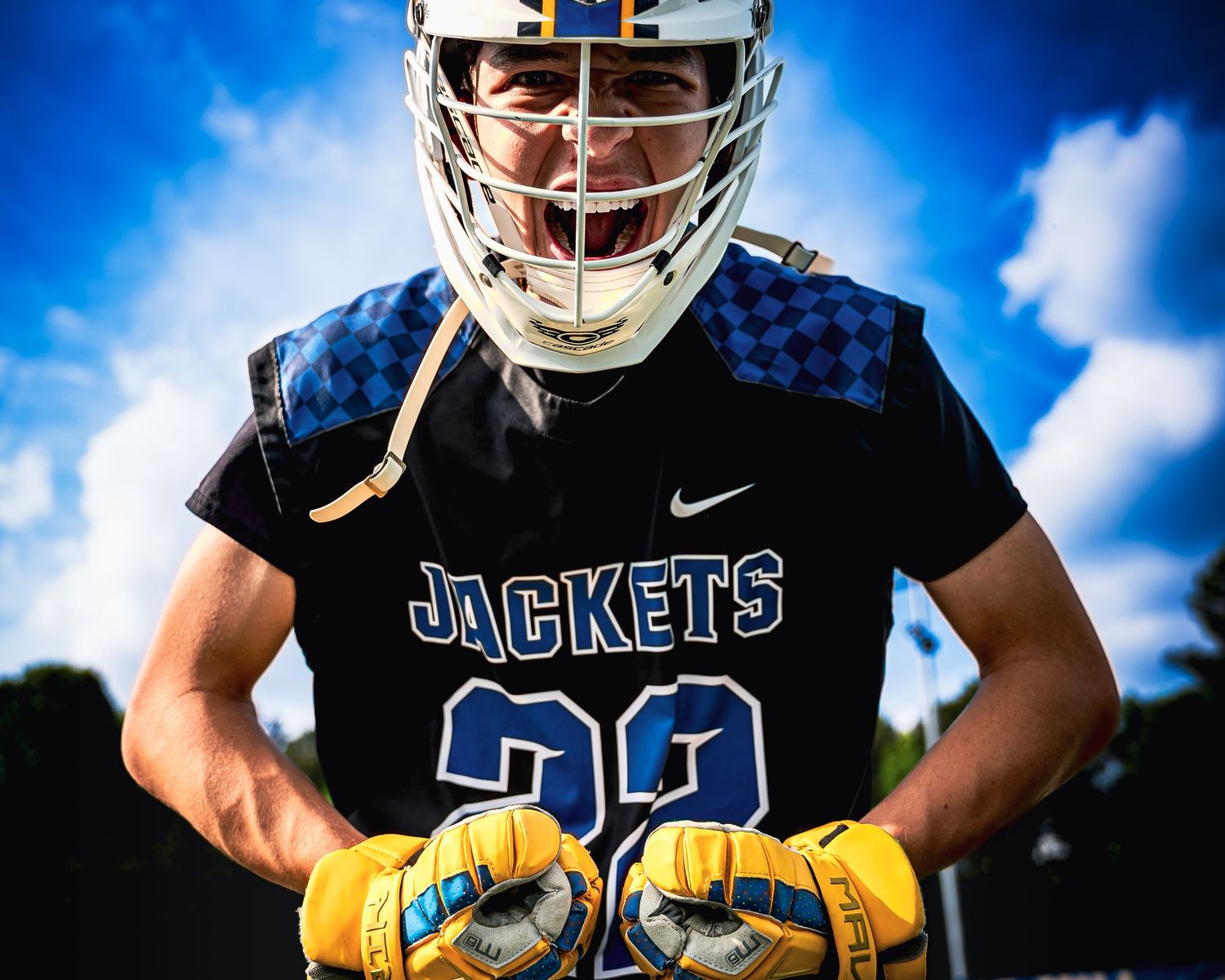 A Fort Mill Yellow Jackets lacrosse player in a black and blue jersey screams in celebration or focus.