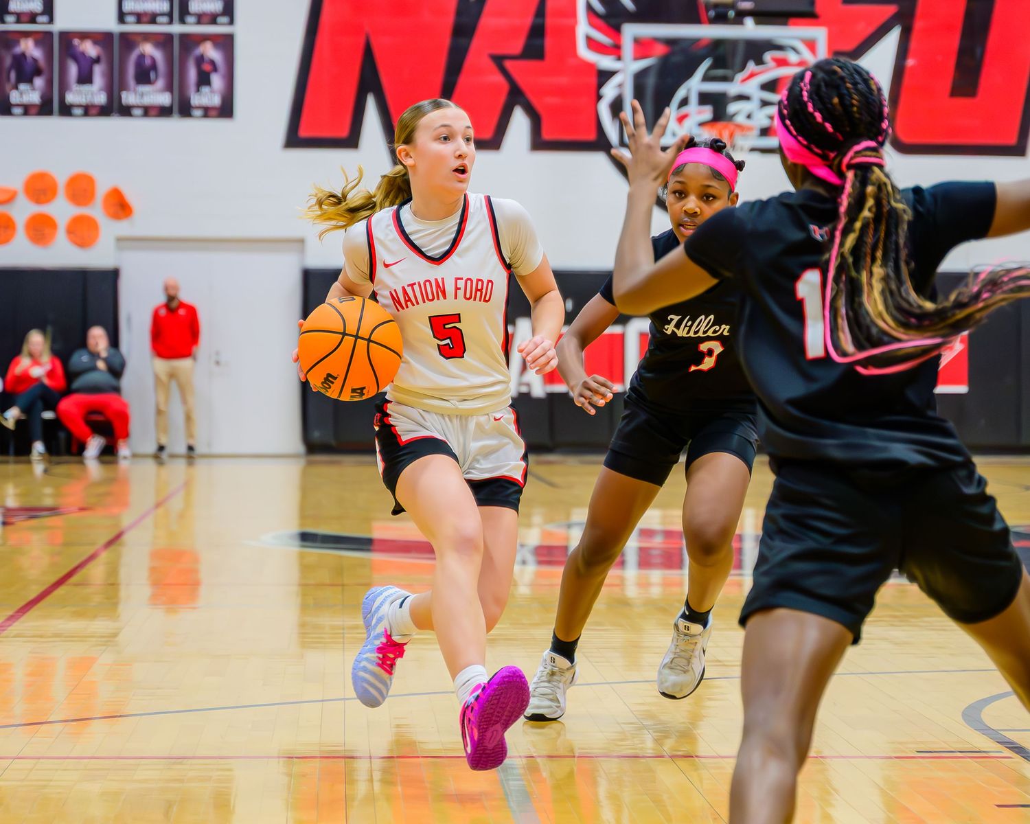 Nation Ford Falcons girls basketball player #5 drives the ball downcourt past defenders during a high school game.