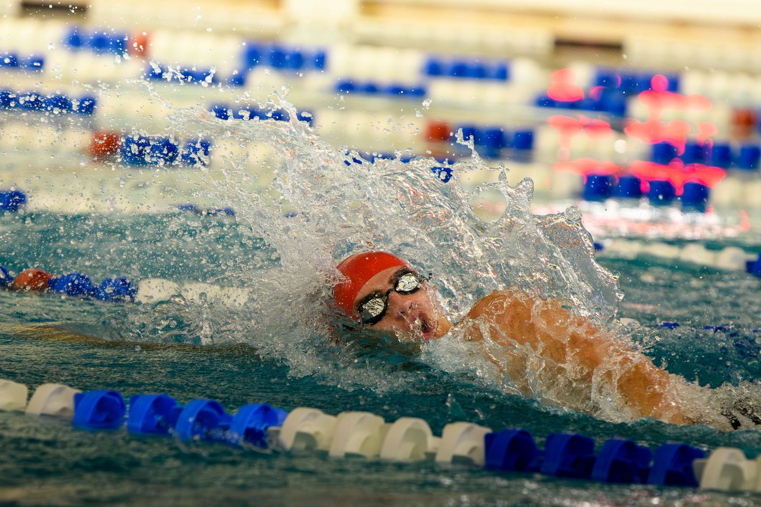 Action shot of a swimmer in a red cap mid-stroke with water splashing around them in a lap pool.