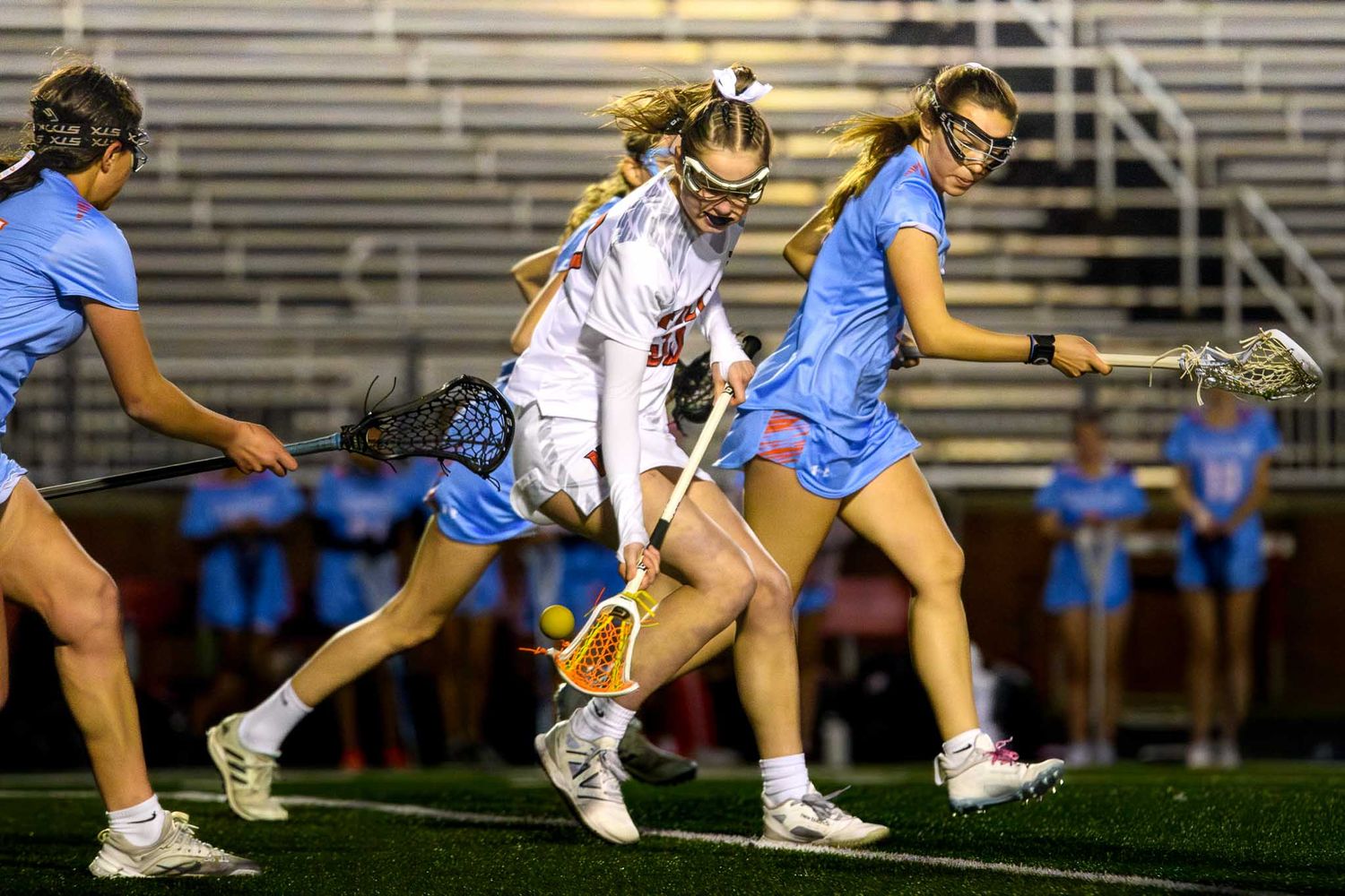 Girls' lacrosse players from Fort Mill and Nation Ford compete for a ground ball during a night game.