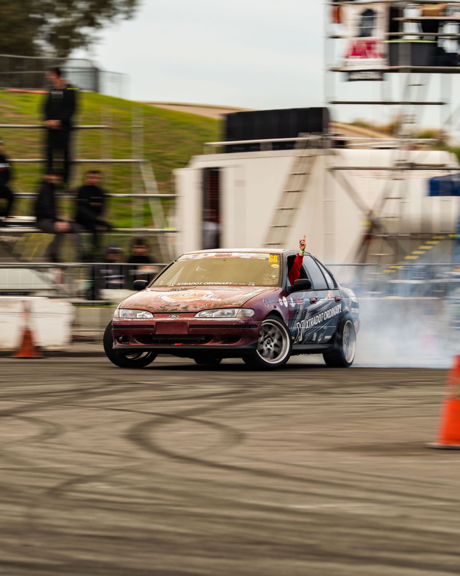 Maroon drift car producing tire smoke on a motorsport circuit.
