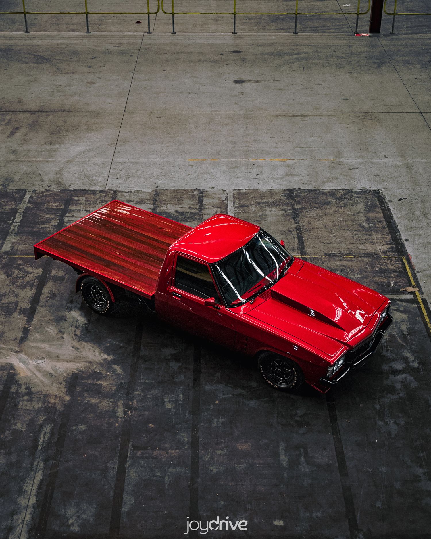 Aerial view of a glossy red classic Holden ute with wooden tray bed on concrete floor.