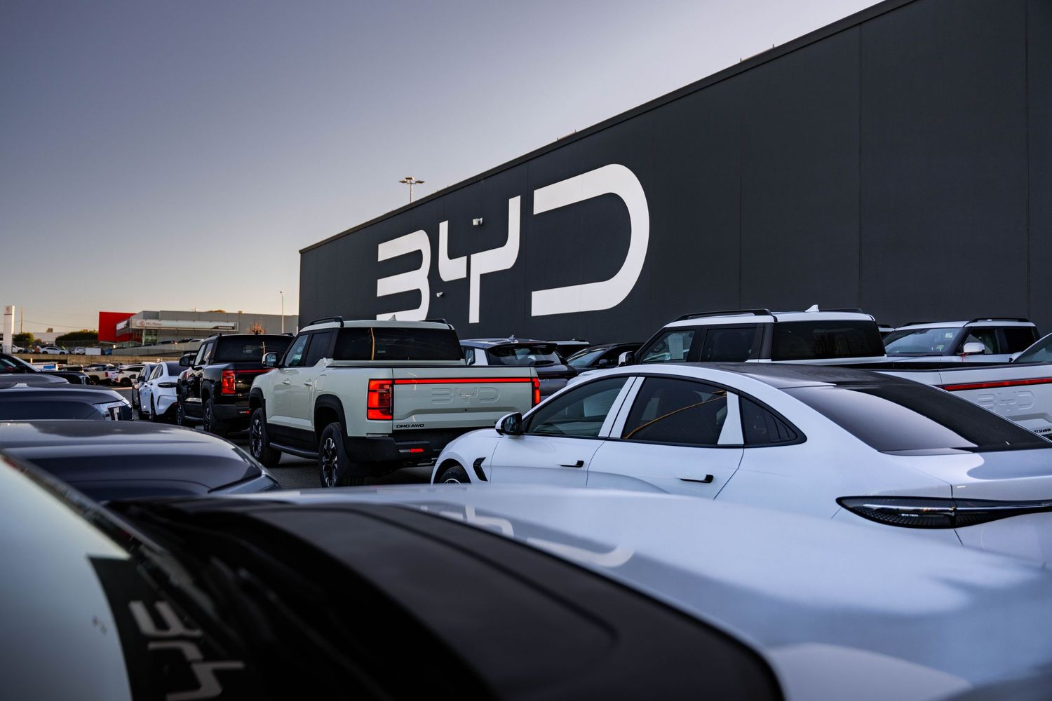 BYD electric vehicle workshop exterior at dusk with large logo and full parking lot.