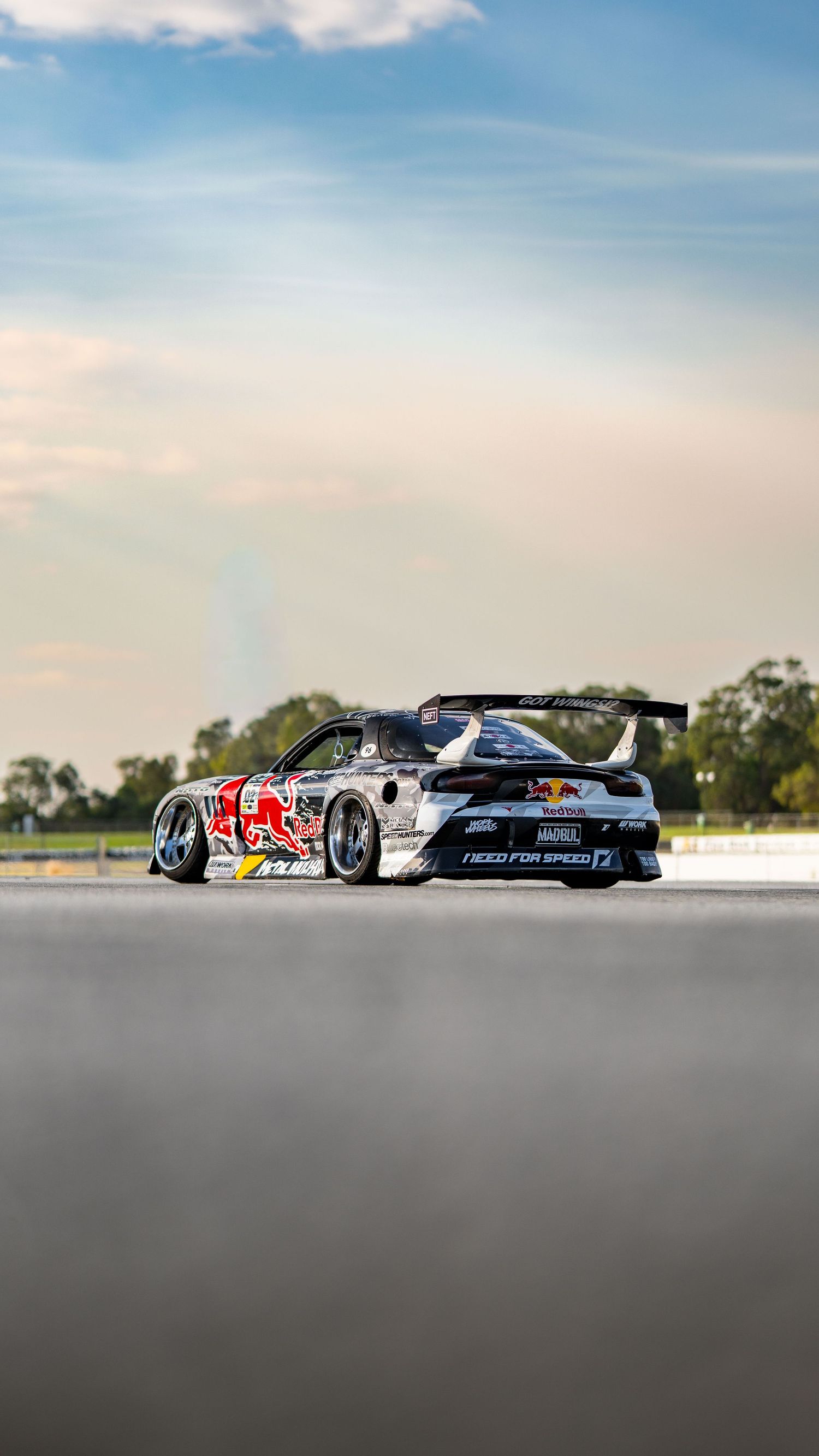 Red Bull and Need for Speed sponsored Mazda RX-7 drift car parked on a racing circuit.