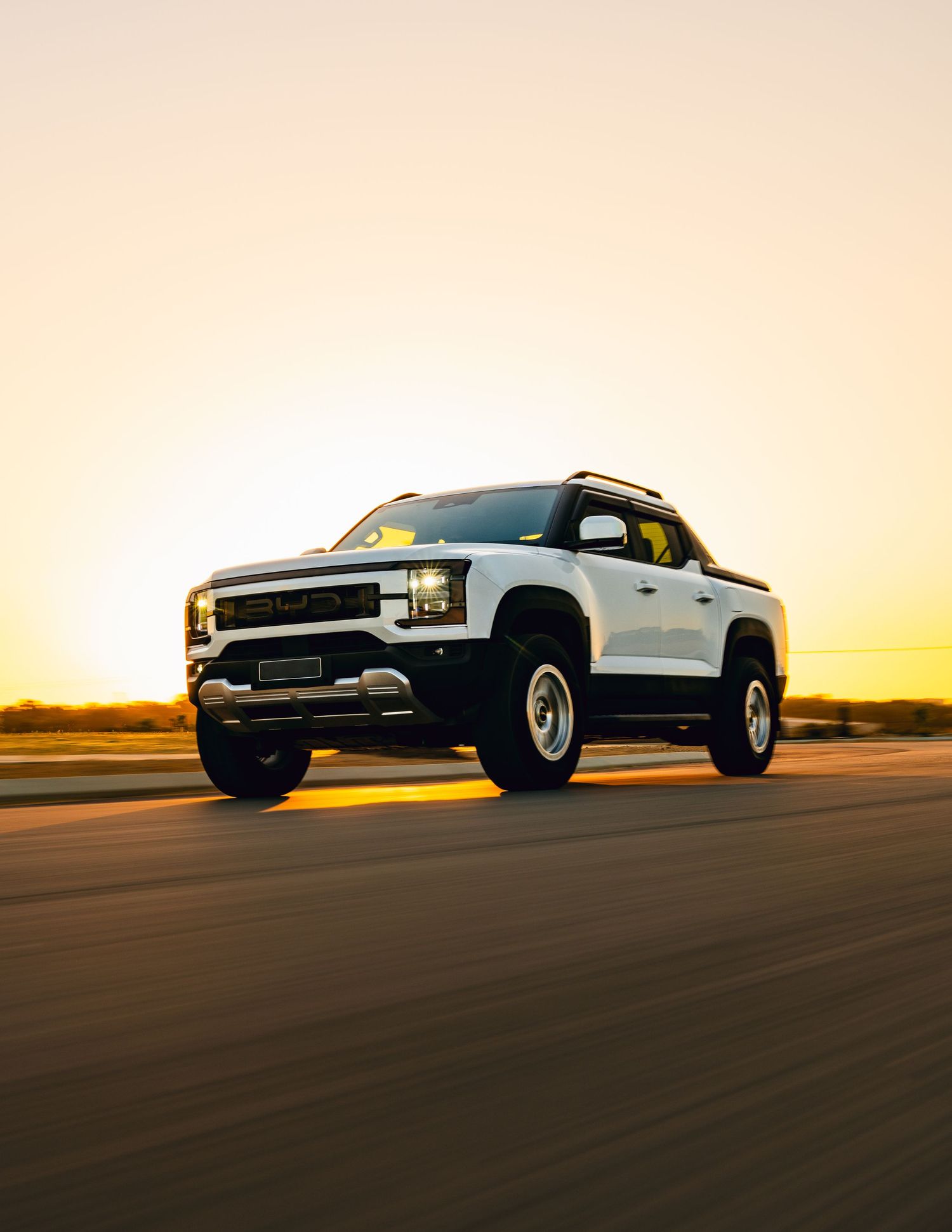 White BYD ute driving at speed on a road during golden hour sunset.