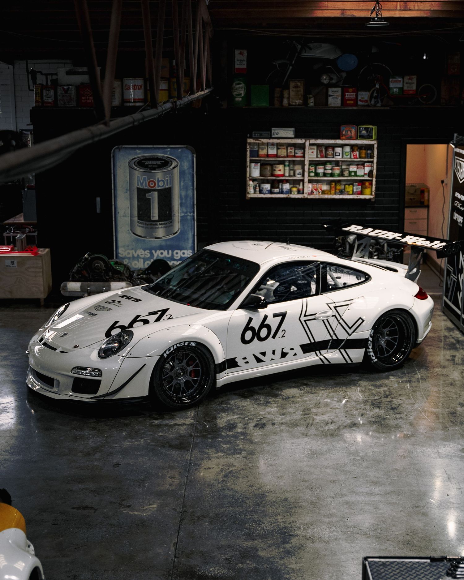 White Porsche 911 GT3 race car number 667 with black graphics parked inside a garage.
