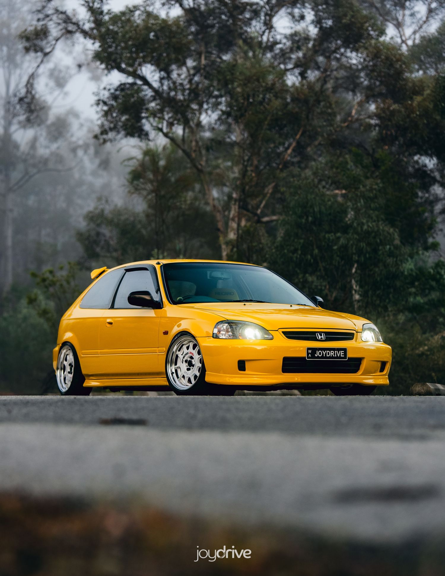 Yellow Honda Civic EK hatchback stance build parked on misty road.