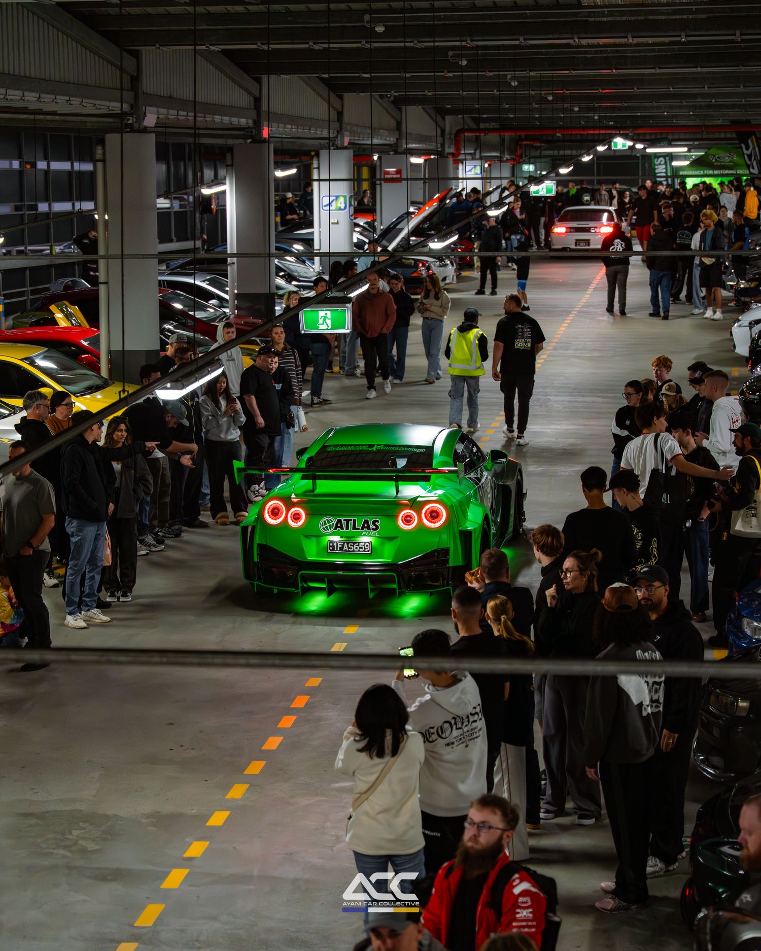 Green Nissan GT-R with neon underglow displayed at a packed underground car show event.