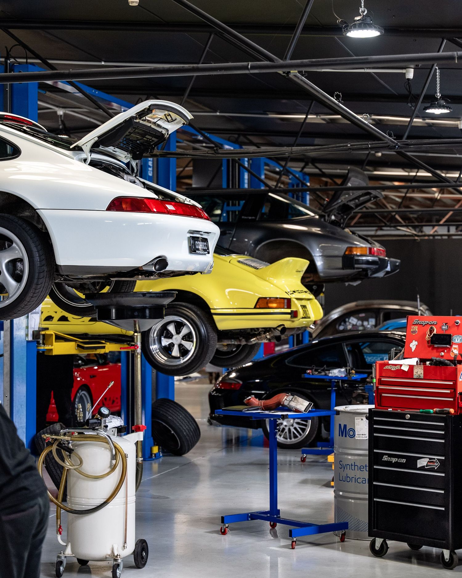 Multiple Porsche 911s on hydraulic lifts inside a professional automotive service workshop.