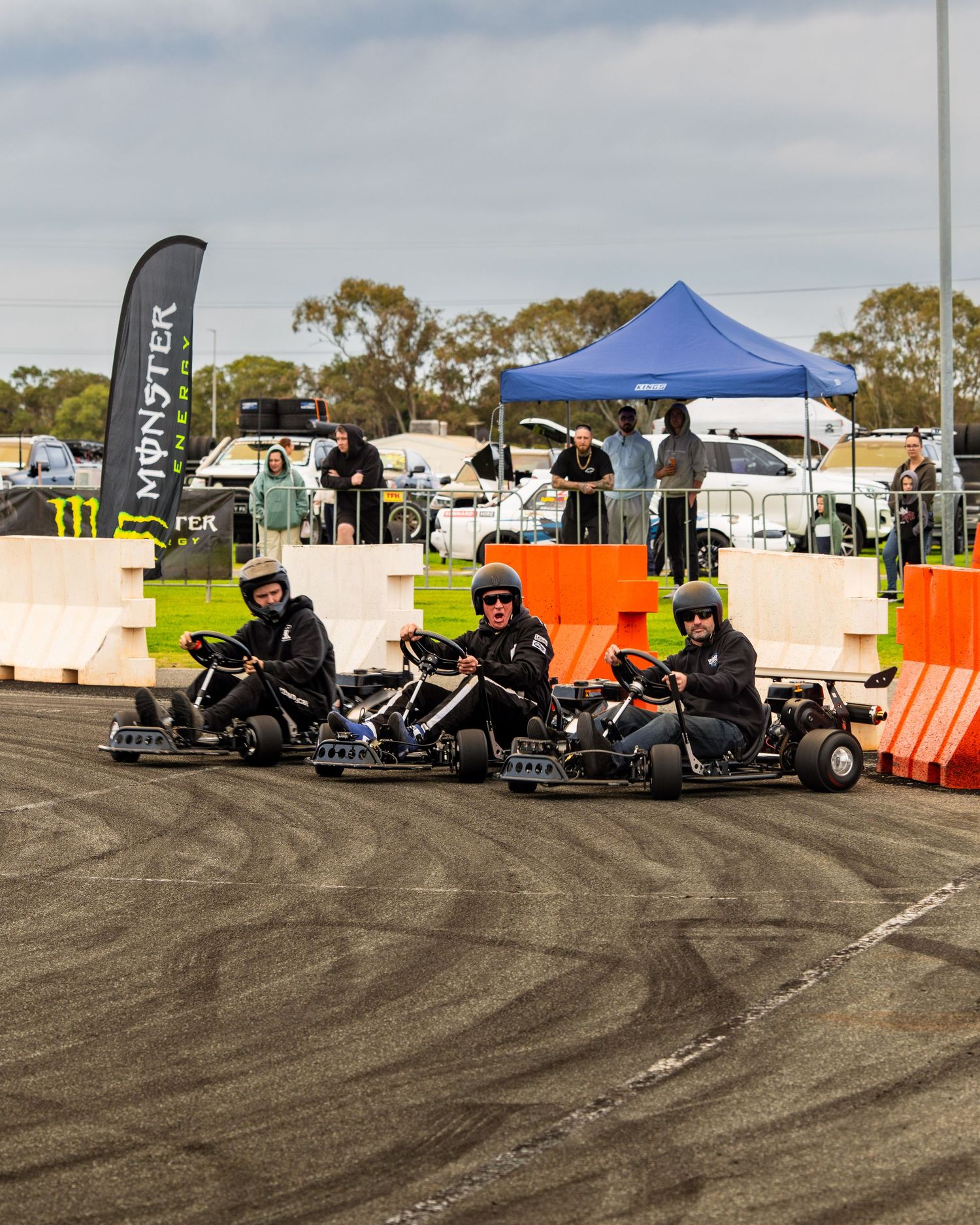 Three go-kart racers cornering on a track at a motorsport event.