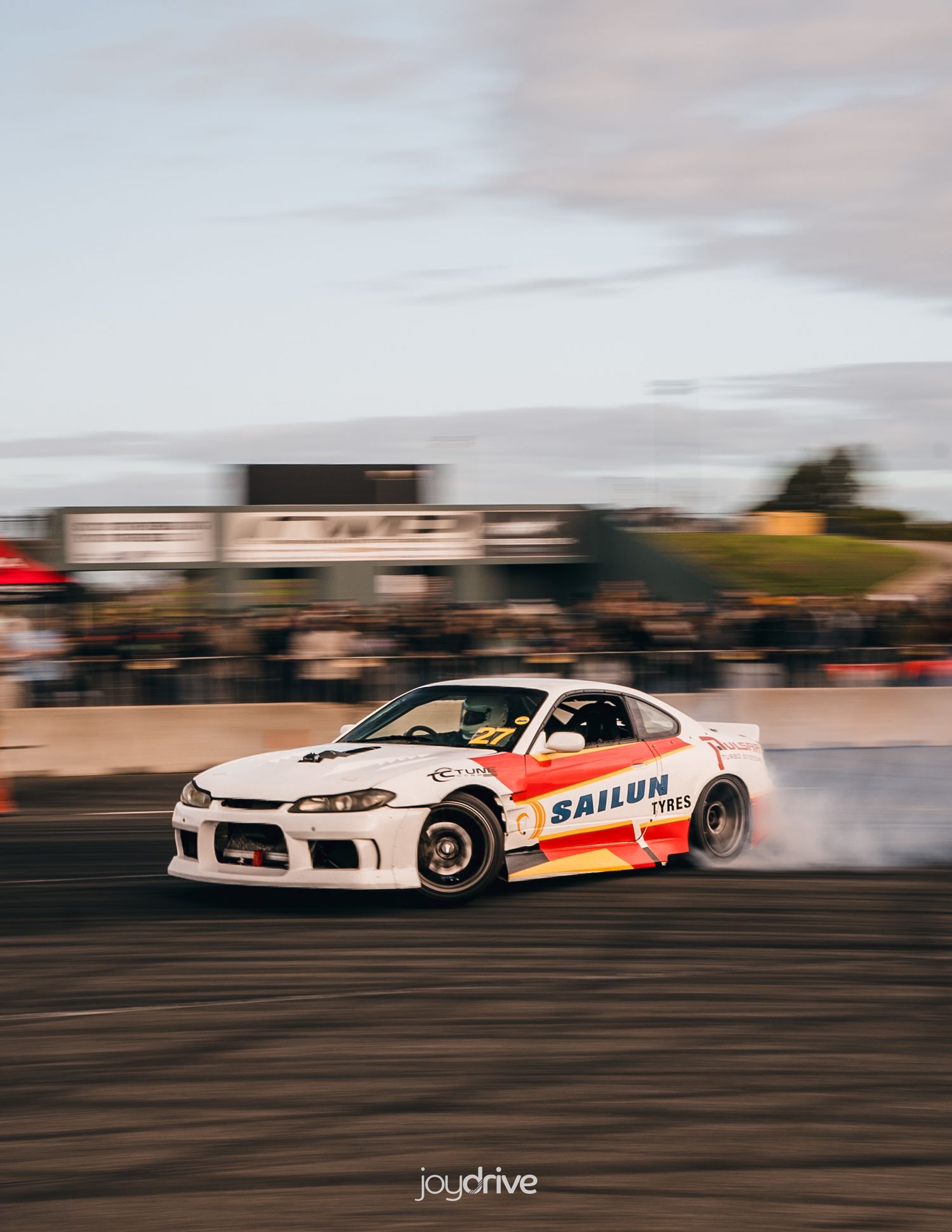 White Nissan Silvia S15 drifting with Sailun Tires livery, producing smoke on a race track.