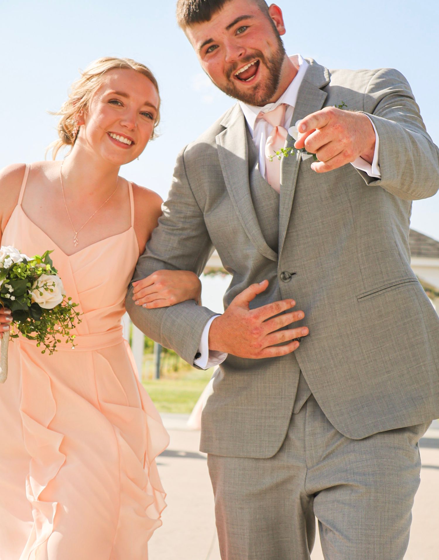 A smiling bridesmaid in peach dress and groomsman in gray suit celebrate joyfully after the ceremony.