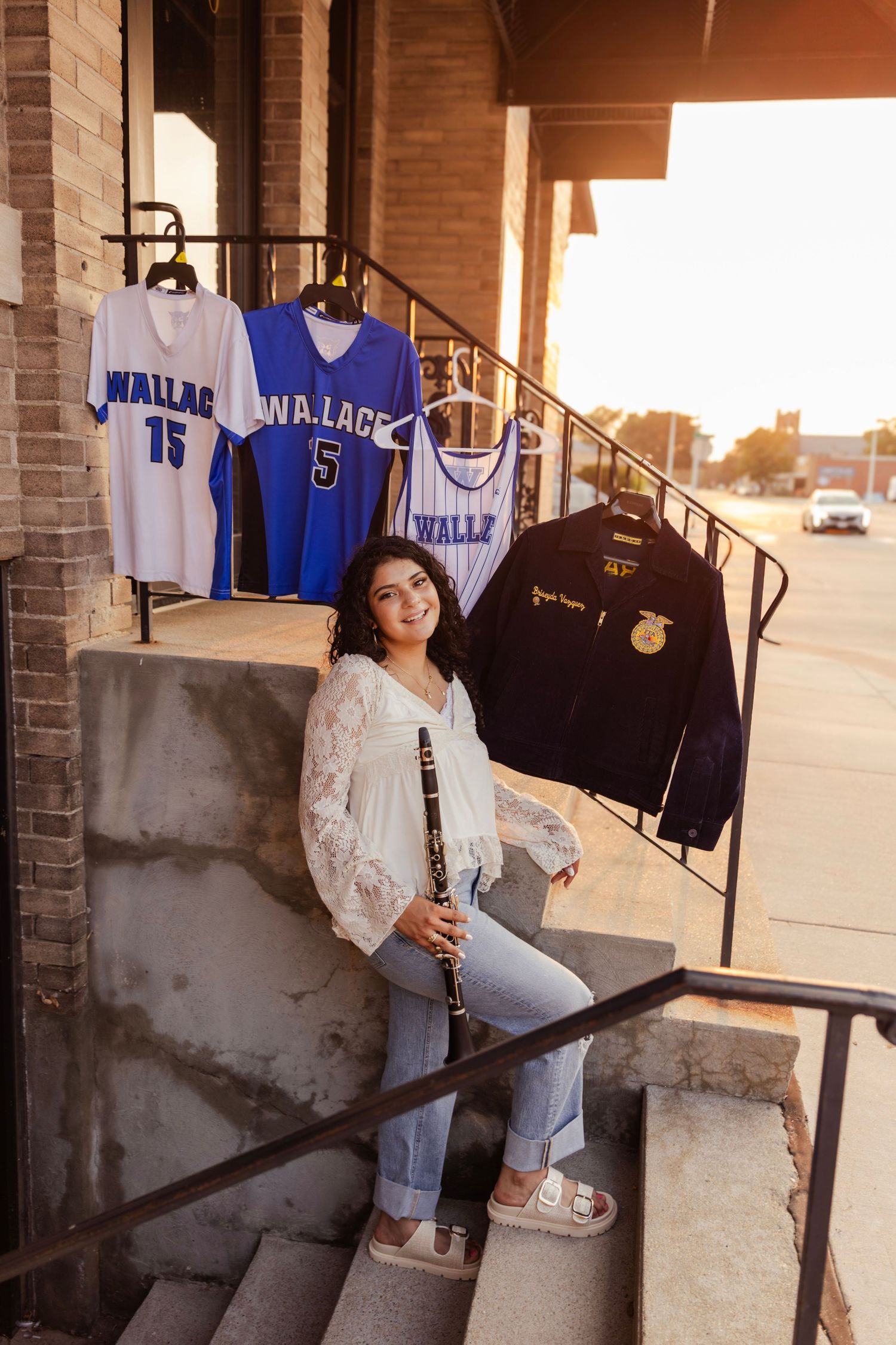 High school senior poses on steps with clarinet and Wallace school jerseys and FFA jacket at golden hour.
