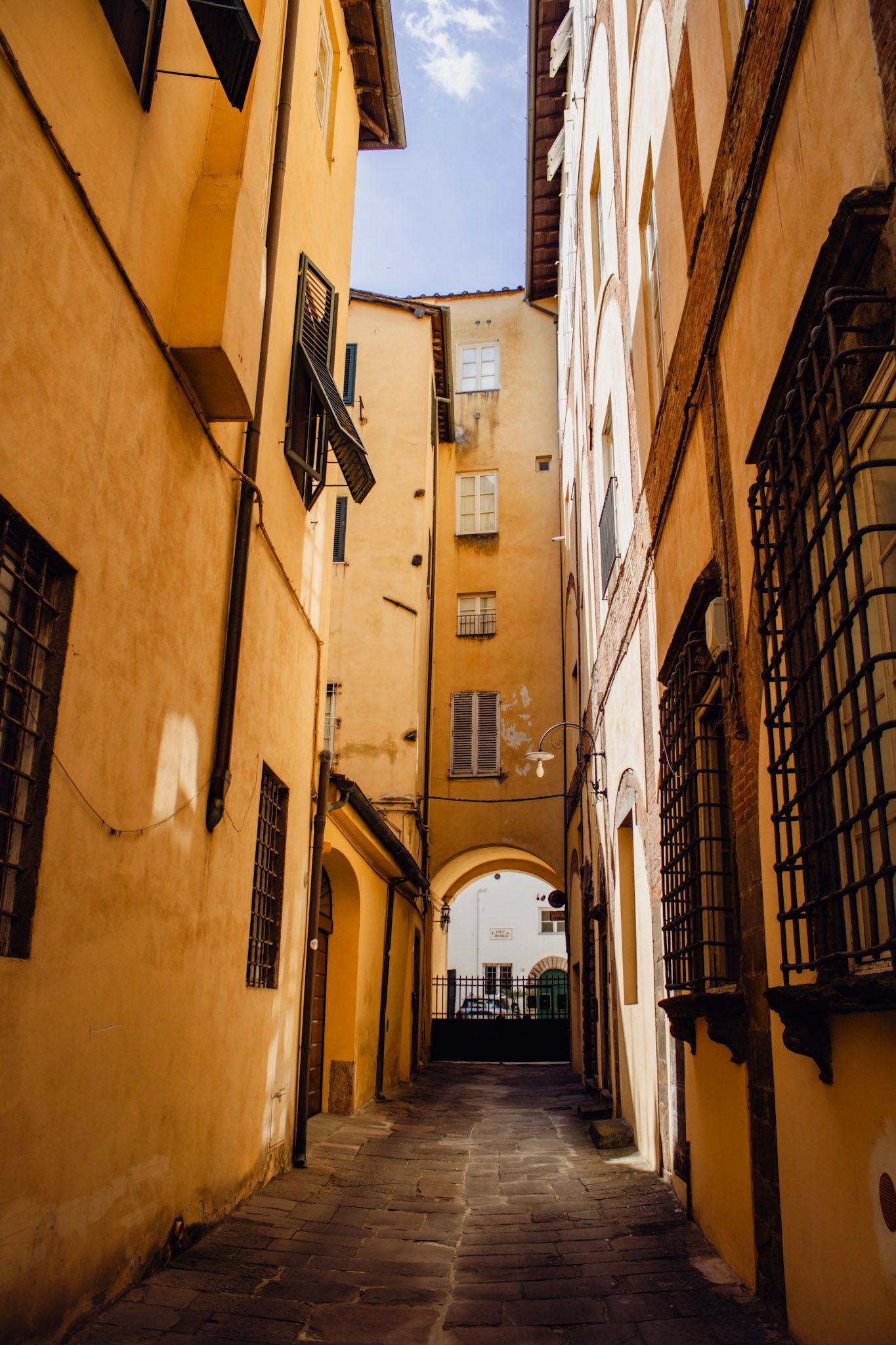 Narrow cobblestone alley flanked by golden-yellow buildings with an arched passage in a historic Italian town.
