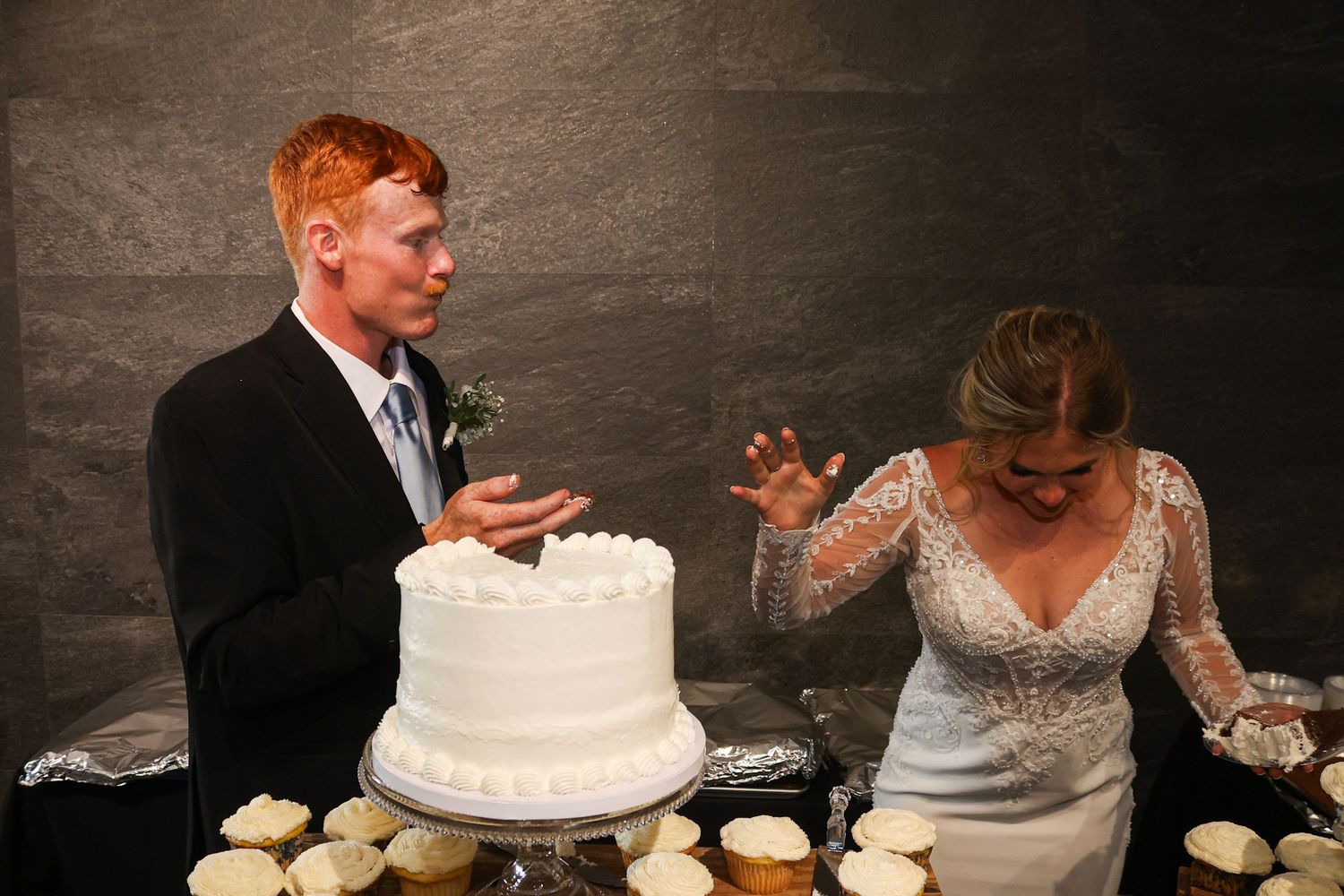 Bride and groom laugh during playful wedding cake cutting moment at their elegant reception.