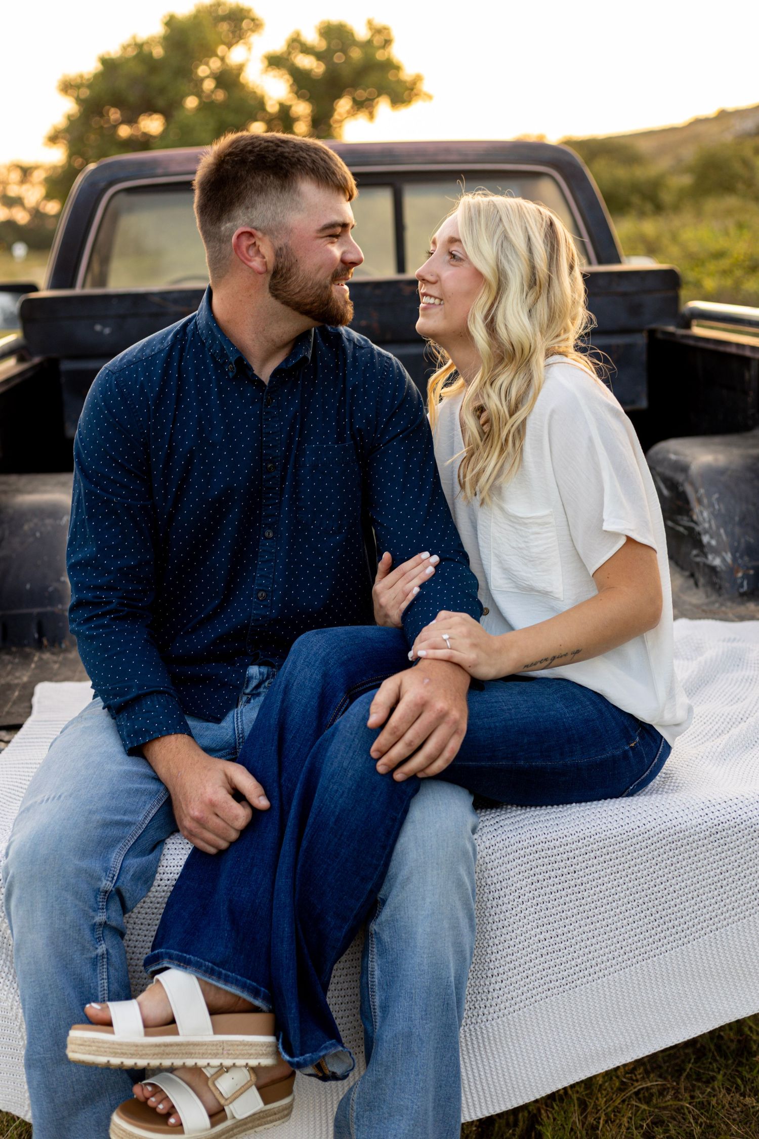 Happy couple gazing at each other seated on truck tailgate at golden hour.