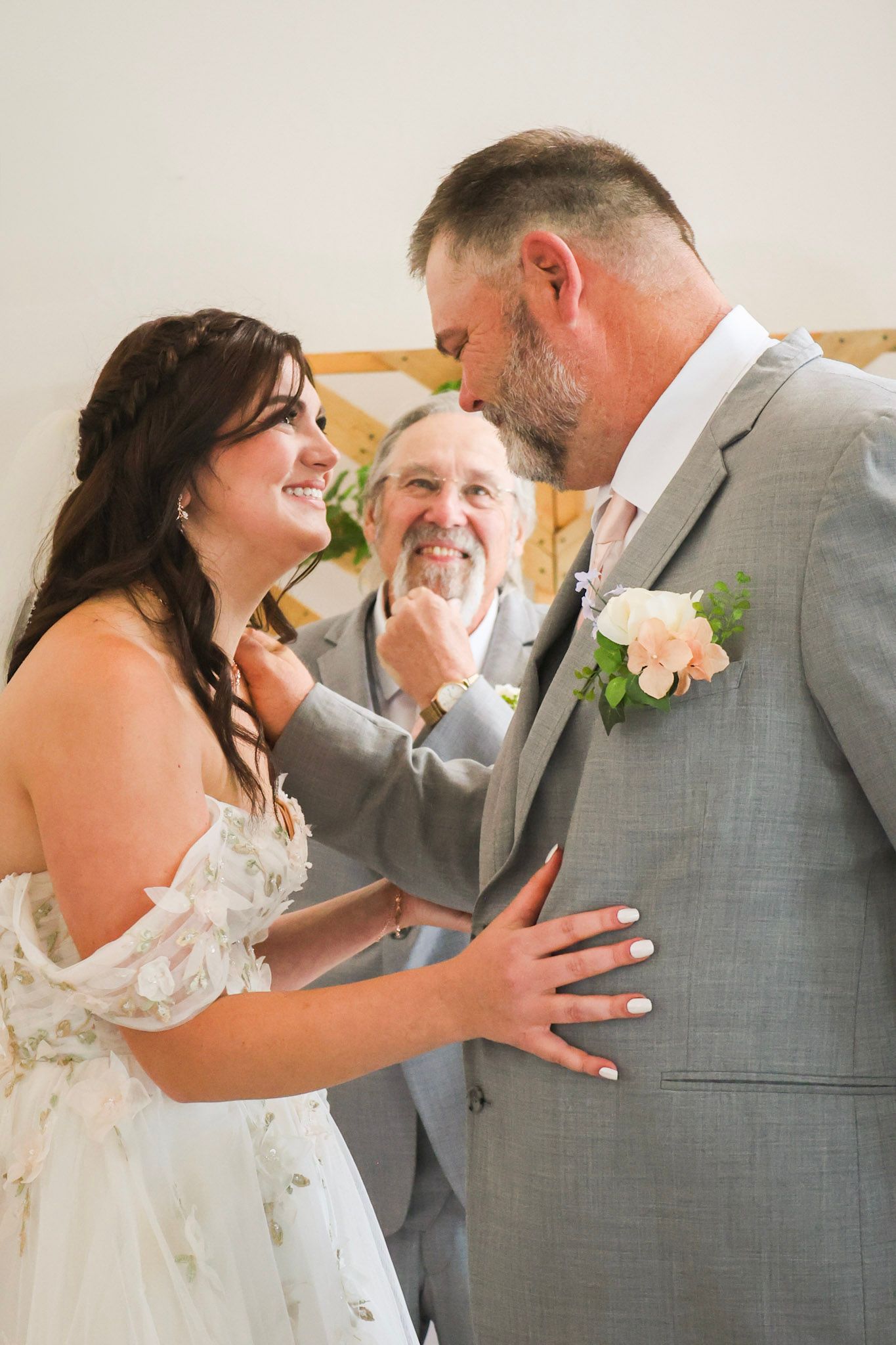 Bride and groom share a joyful moment during wedding ceremony as officiant smiles in background.
