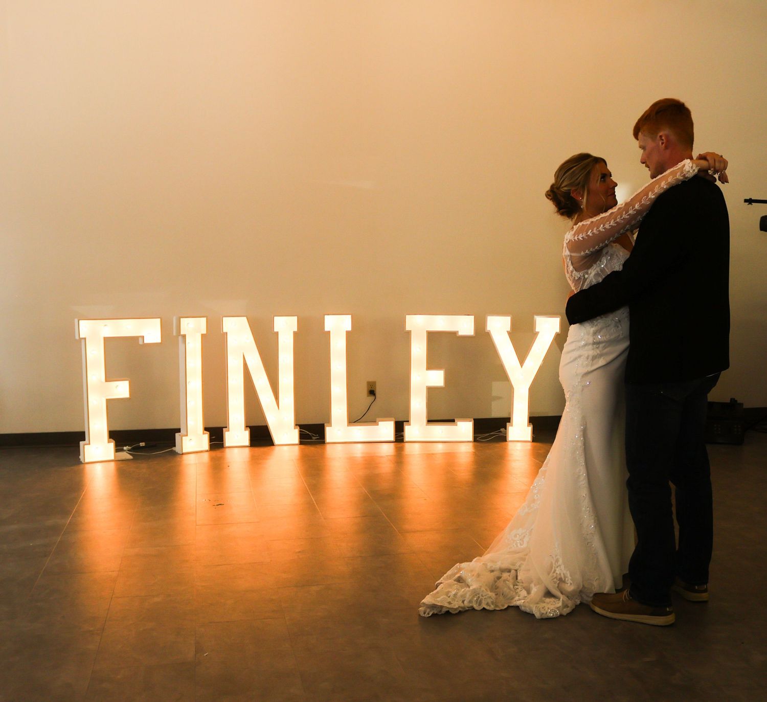 Bride and groom share first dance in front of large illuminated FINLEY marquee letters at reception.